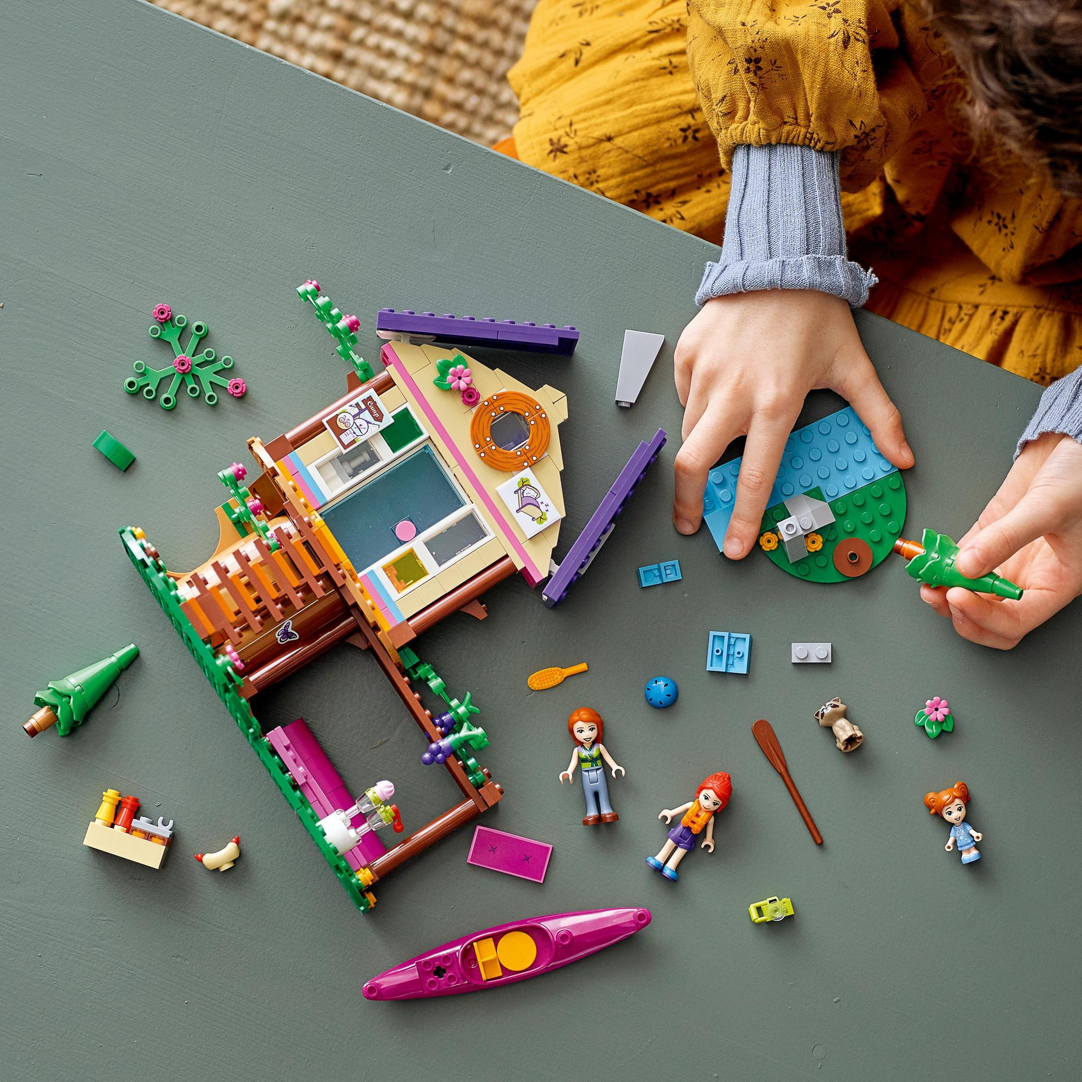 Çocuk LEGO Friends setini bir araya getiriyor. Set bir ev, figürler ve çeşitli renkli parçalar içerir.