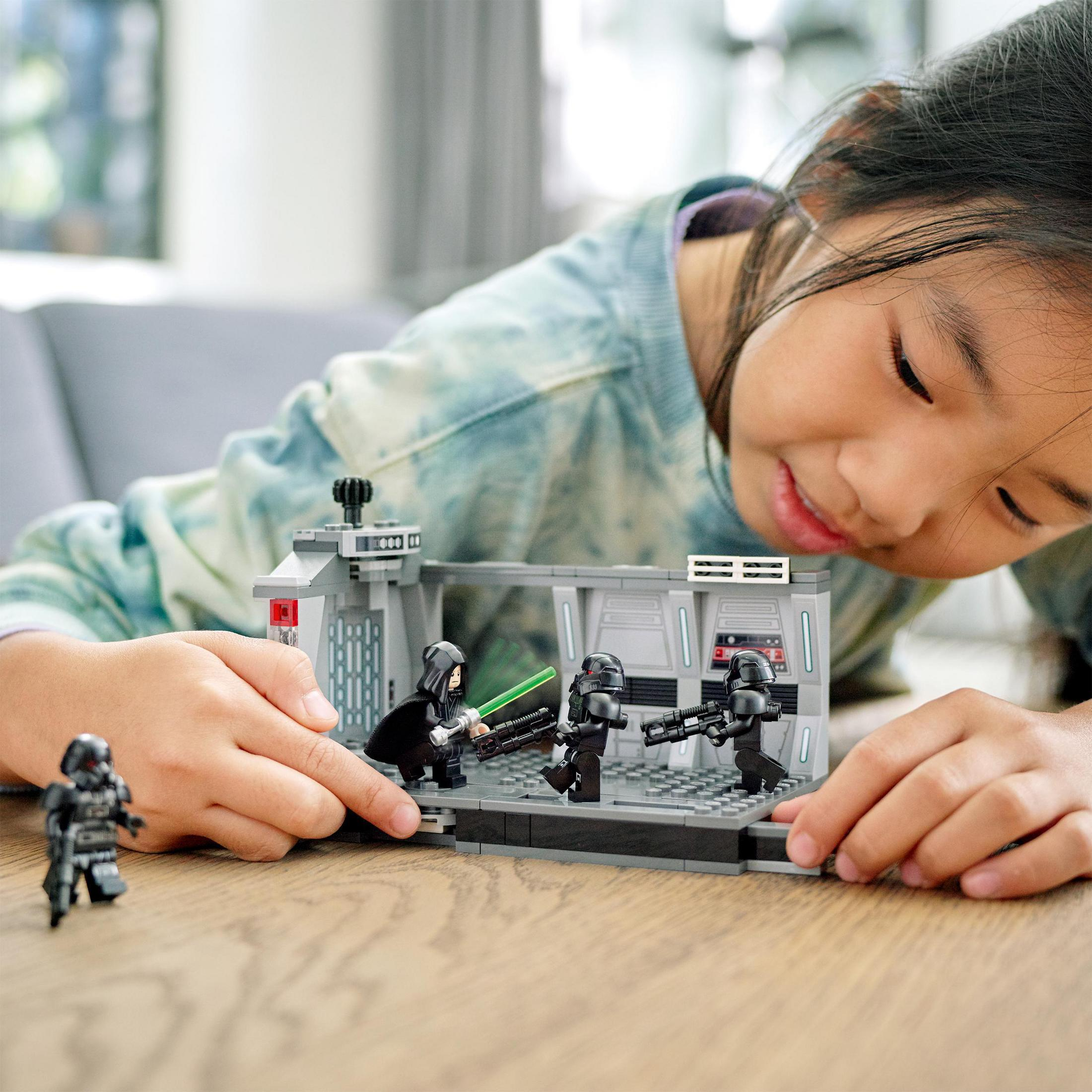 Mädchen betrachtet Lego Star Wars Set mit Figuren, dunkle Figur mit grünem Lichtschwert.