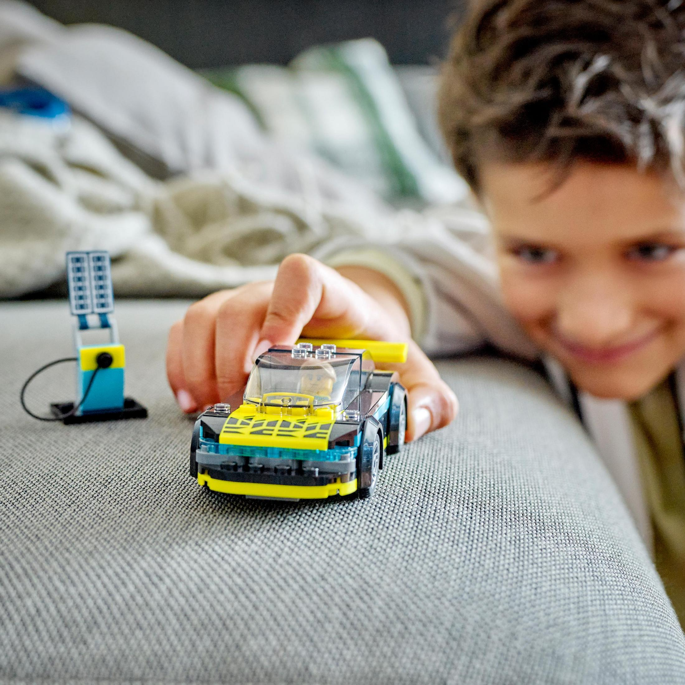 Çocuk Lego yarış arabası oyuncağıyla oynuyor. Arka planda bir benzin pompası oyuncağı.