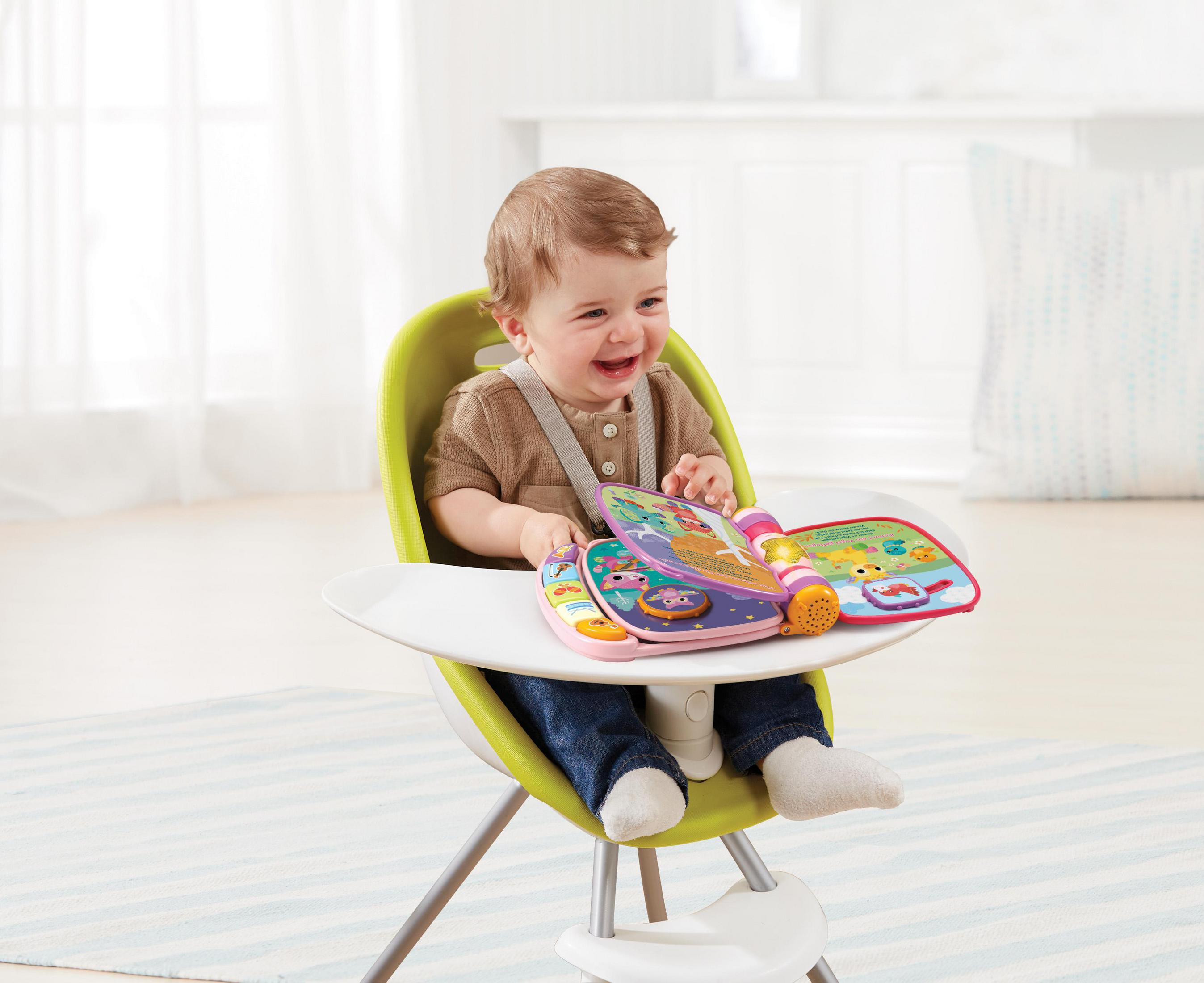 Ein Baby sitzt in einem grünen Stuhl und schaut sich ein rosa Buch an.