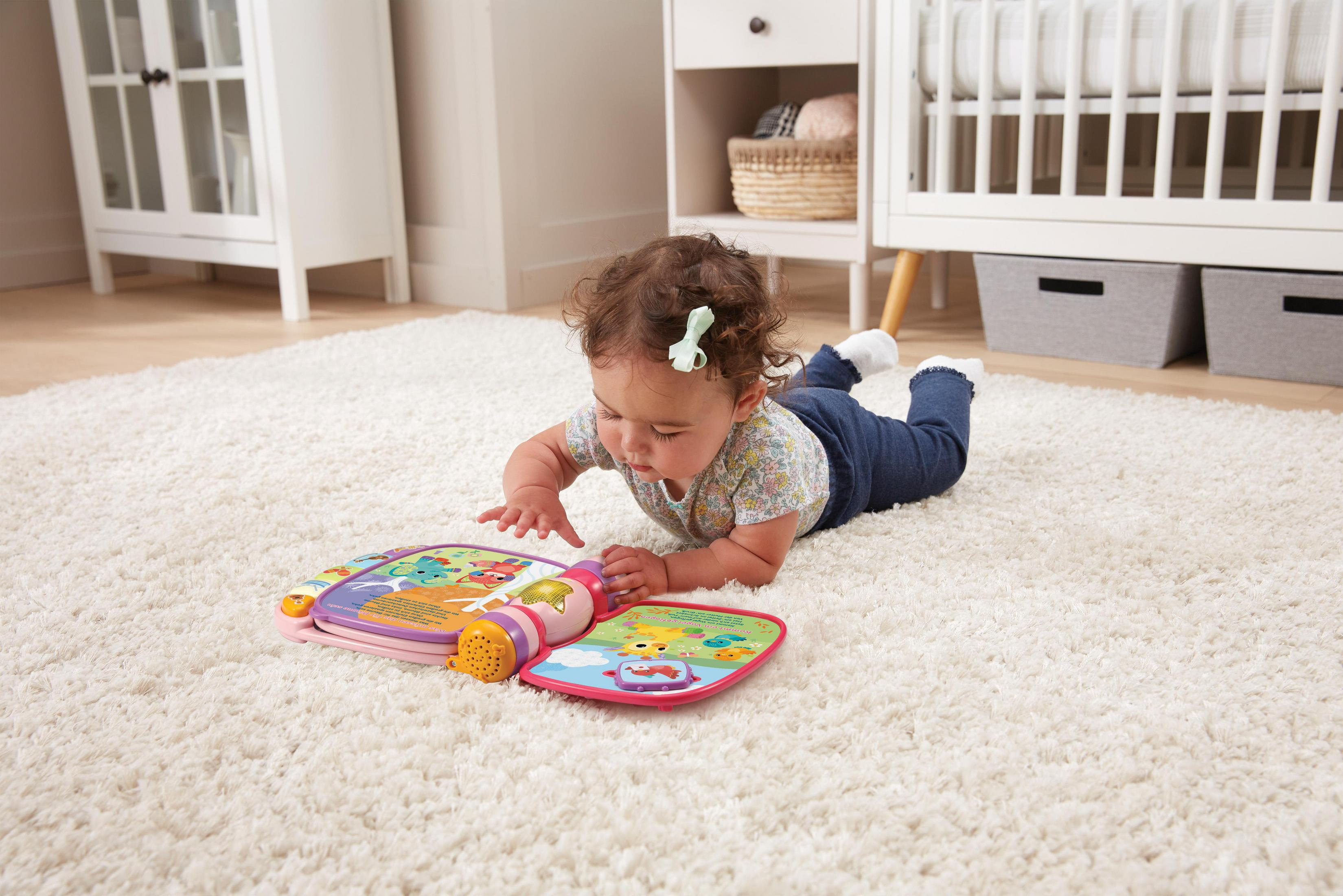 Ein Baby liegt auf einem flauschigen weißen Teppich und spielt mit einem rosa Buch.