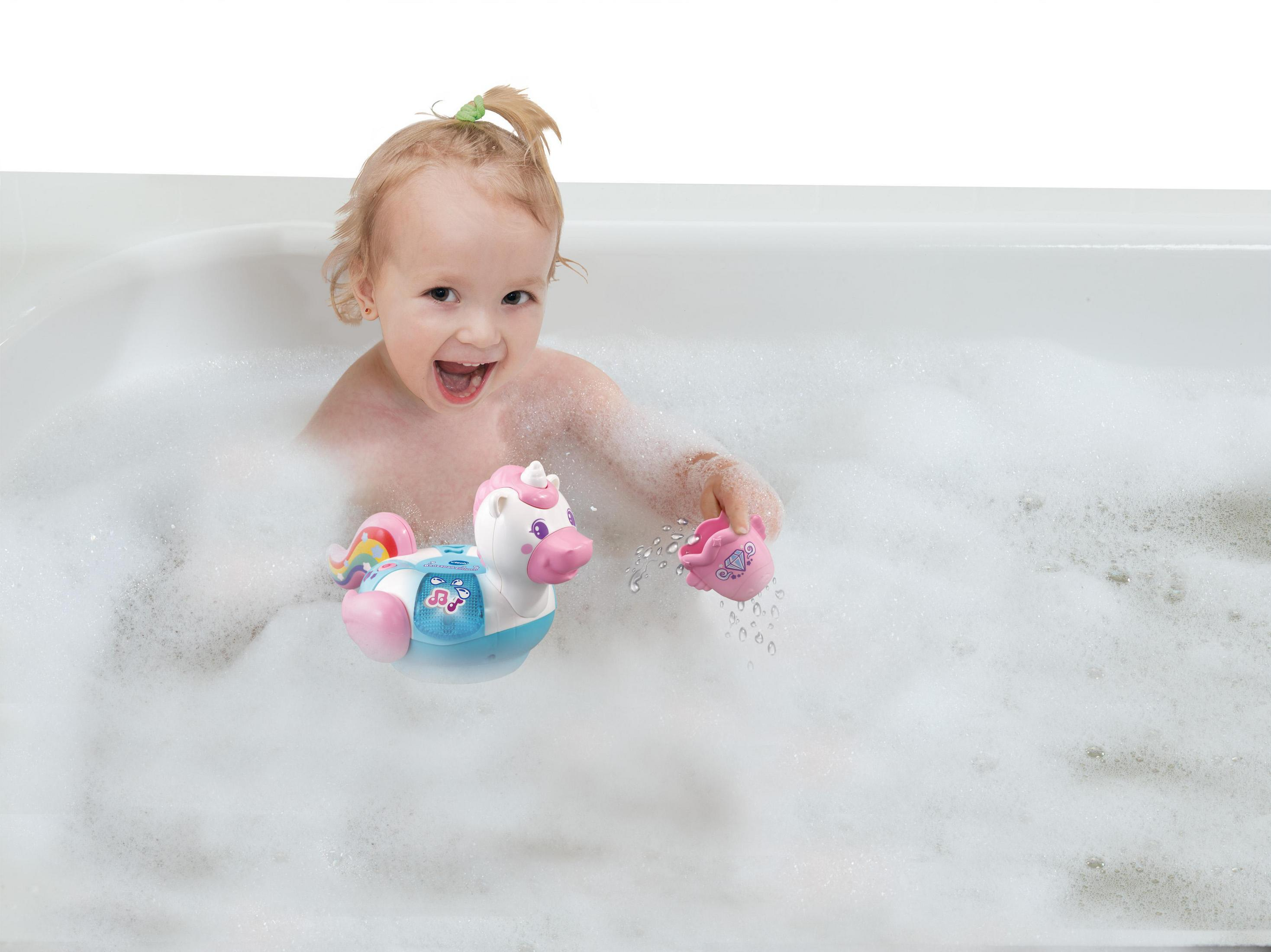 Ein Kleinkind in einer Badewanne mit Blasen. Sie spielt mit einem Spielzeug-Einhorn und anderem Badespielzeug.