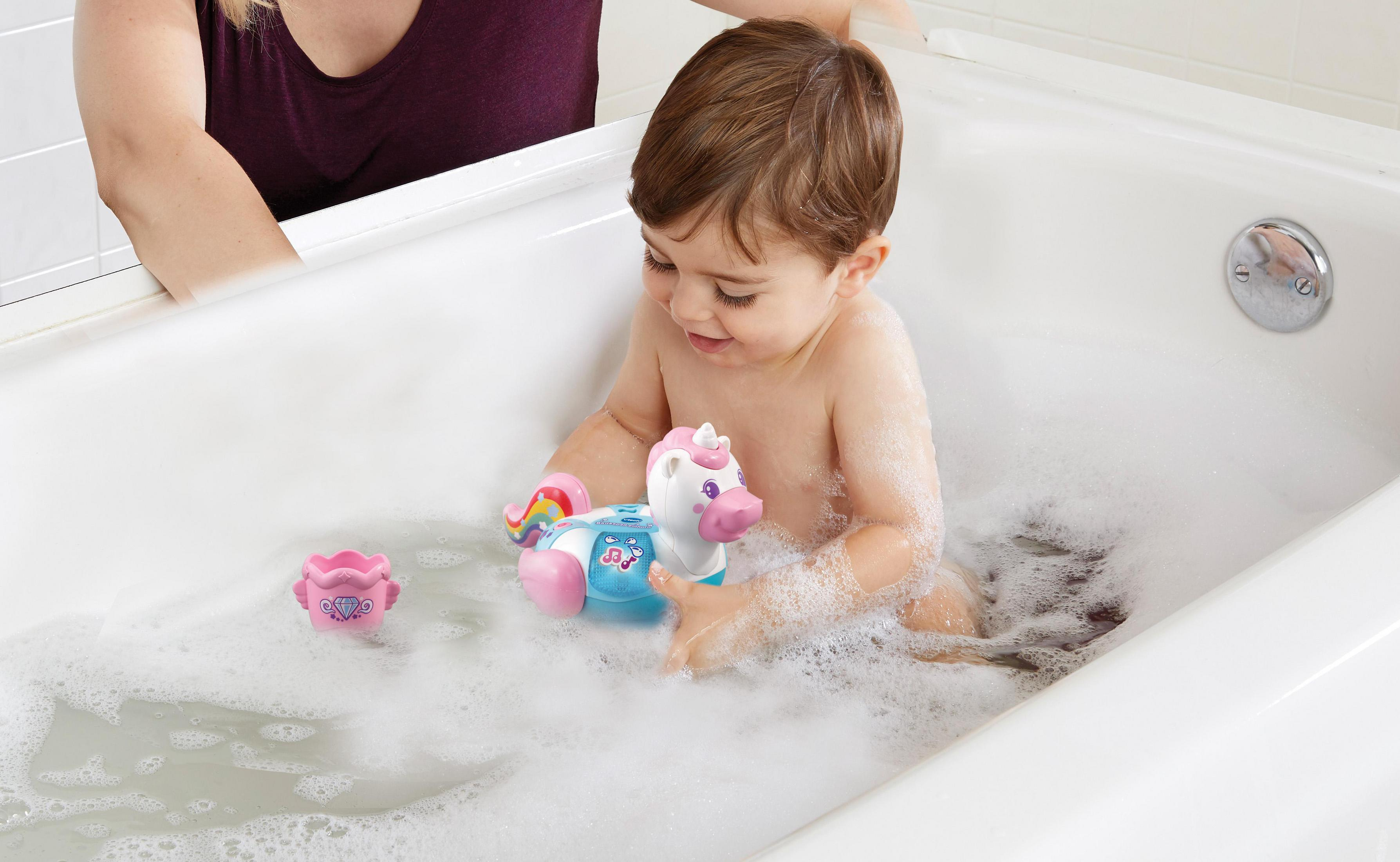Ein Baby in einer Badewanne mit einem Einhornspielzeug. Schaum ist vorhanden.