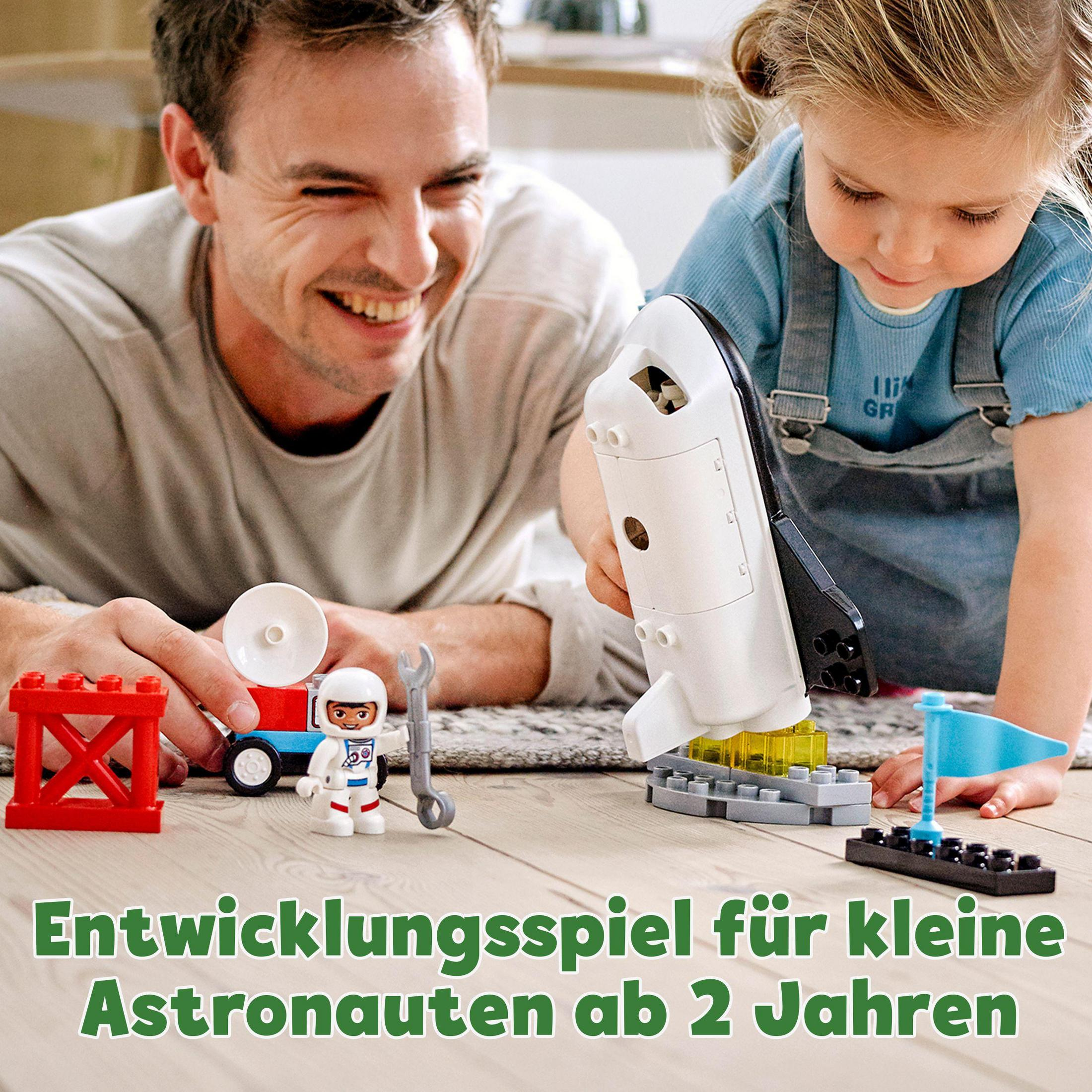 Ein Vater und eine Tochter spielen mit einem Lego-Weltraumschiff-Set auf Holzboden, mit Text.