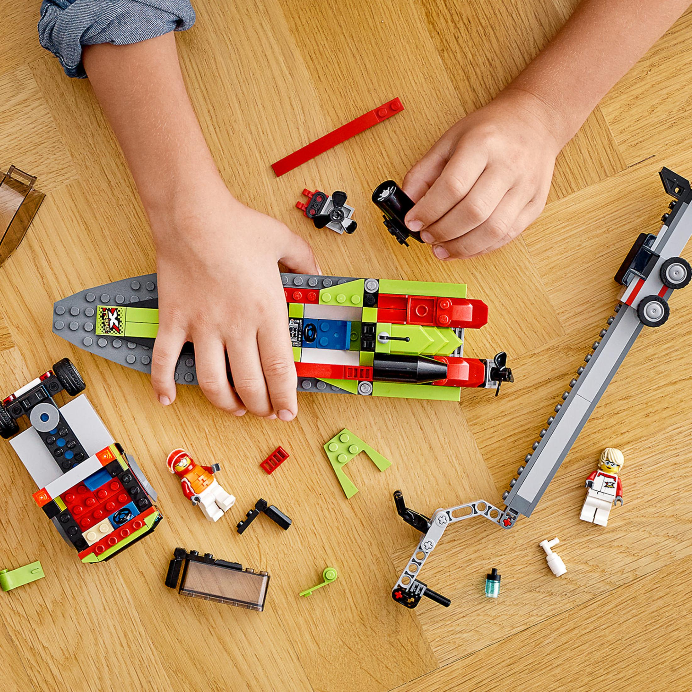 Mani di bambino che giocano con i Lego: Barca, auto e vari pezzi Lego su una superficie di legno.