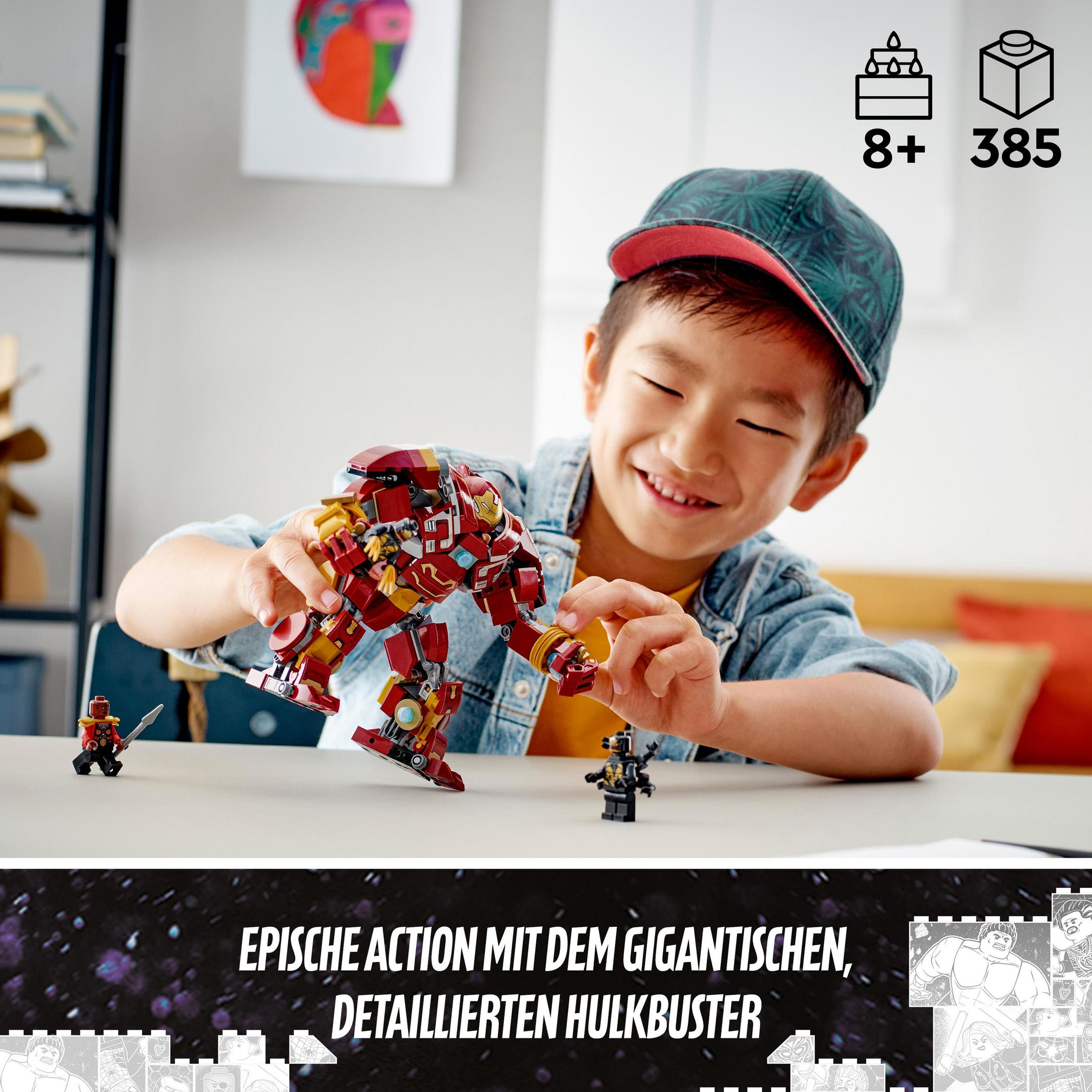 Ein Junge spielt mit einem Lego Hulkbuster-Set. Das Set ist rot und gold, mit kleinen Figuren und einem schwarzen Tisch.