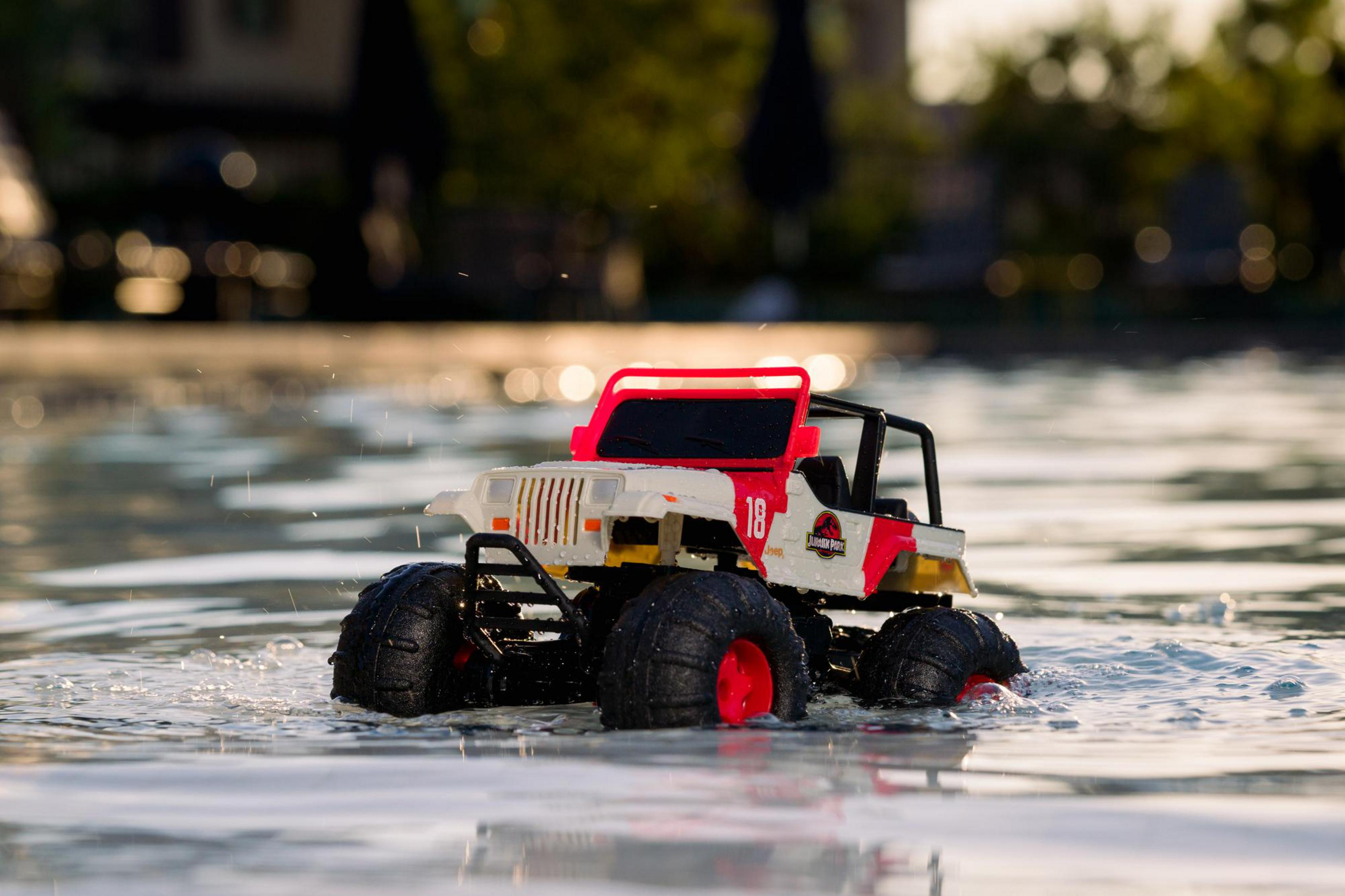 Spielzeug-Jeep im Wasser. Weißer Körper, rote Akzente, schwarze Reifen. Spiegelungen im Wasser.