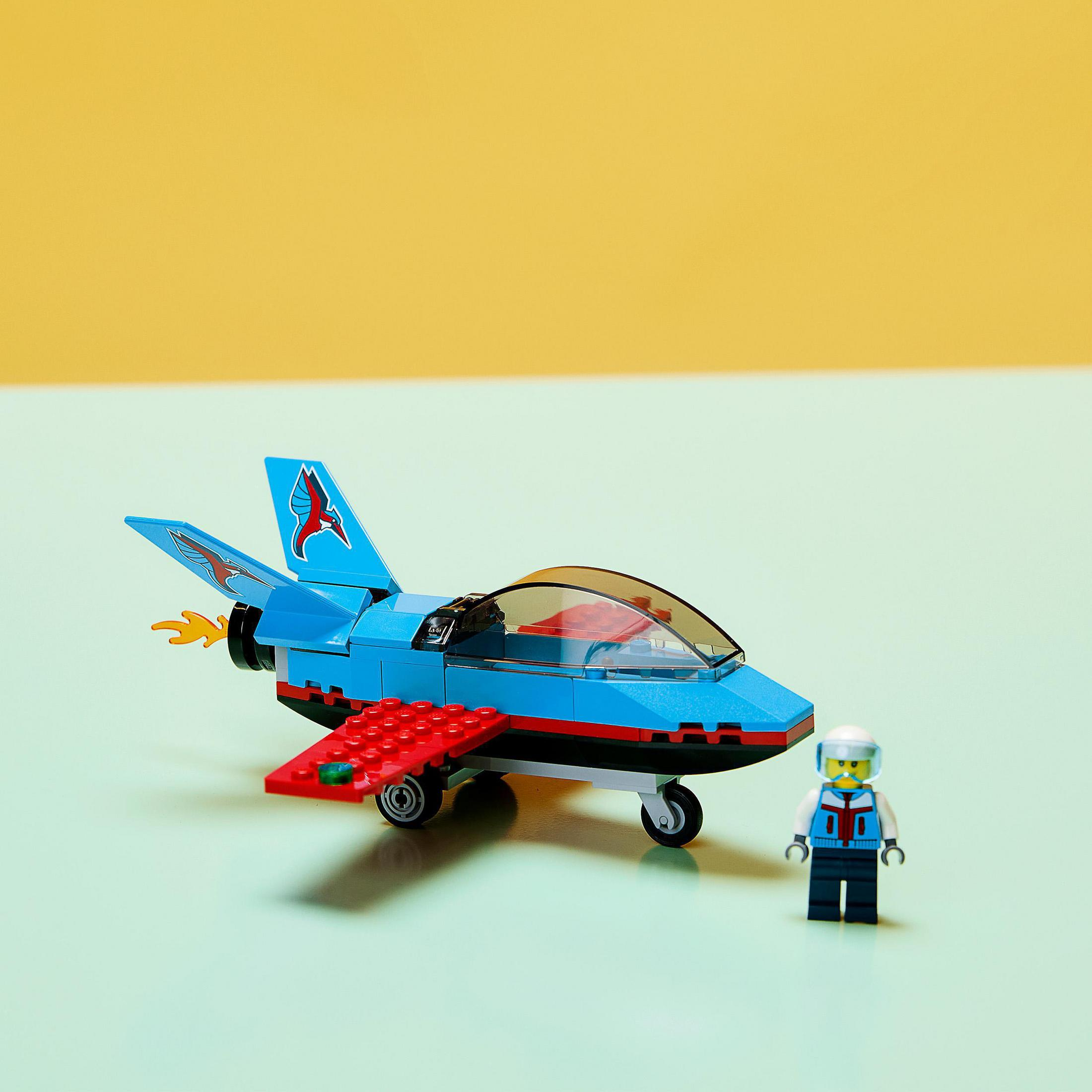 Ein blaues und rotes Spielzeug-Düsenflugzeug mit einer Pilotenfigur vor gelbem und hellgrünem Hintergrund.