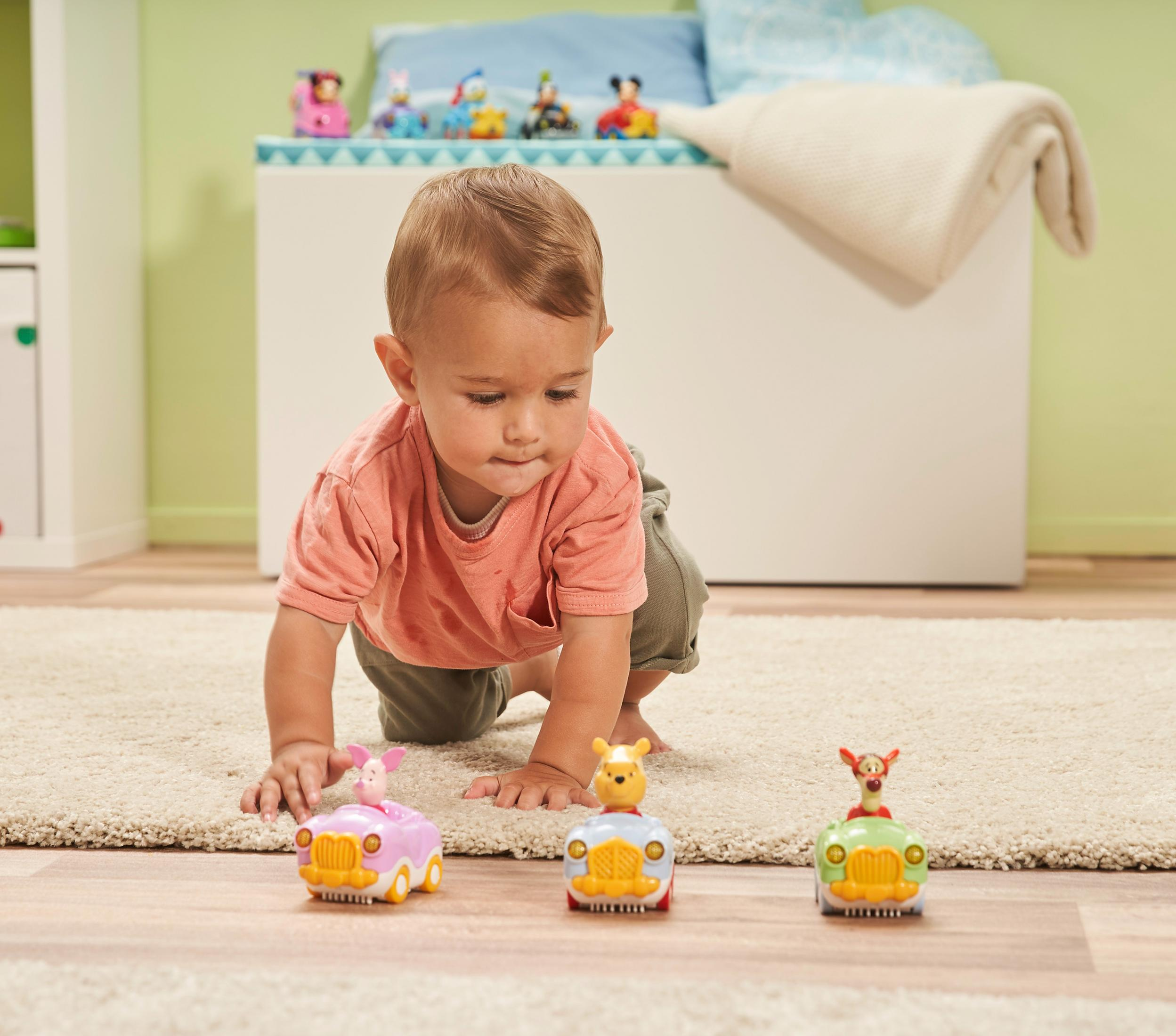 Baby spielt mit Spielzeugautos. Winnie Puuh, Ferkel und Tigger sind auf den Autos.