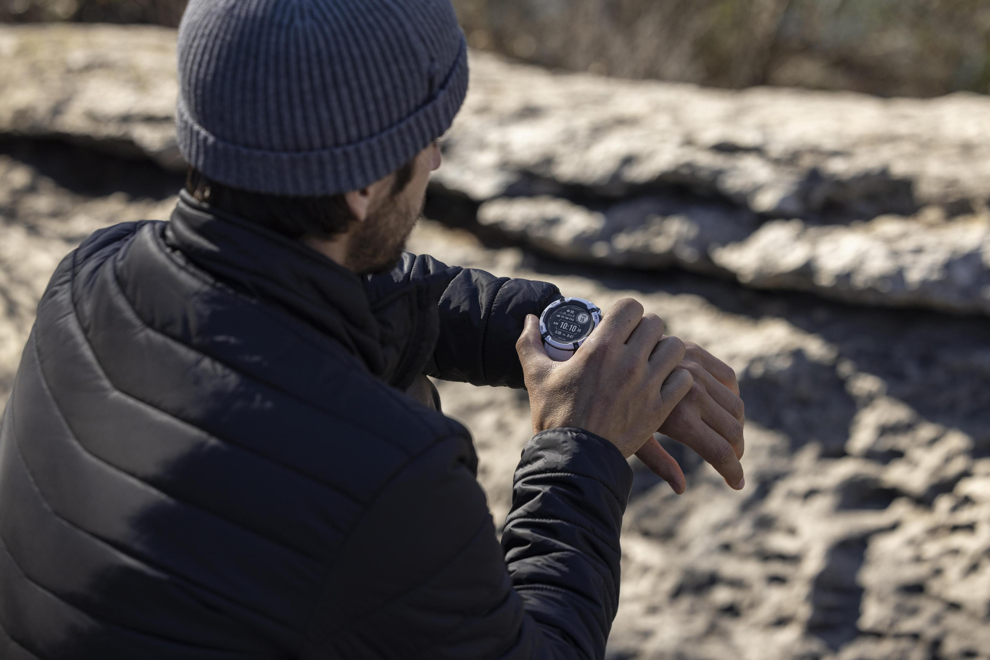 Mann, der draußen auf seine Smartwatch am Handgelenk schaut. Felsiger Hintergrund.