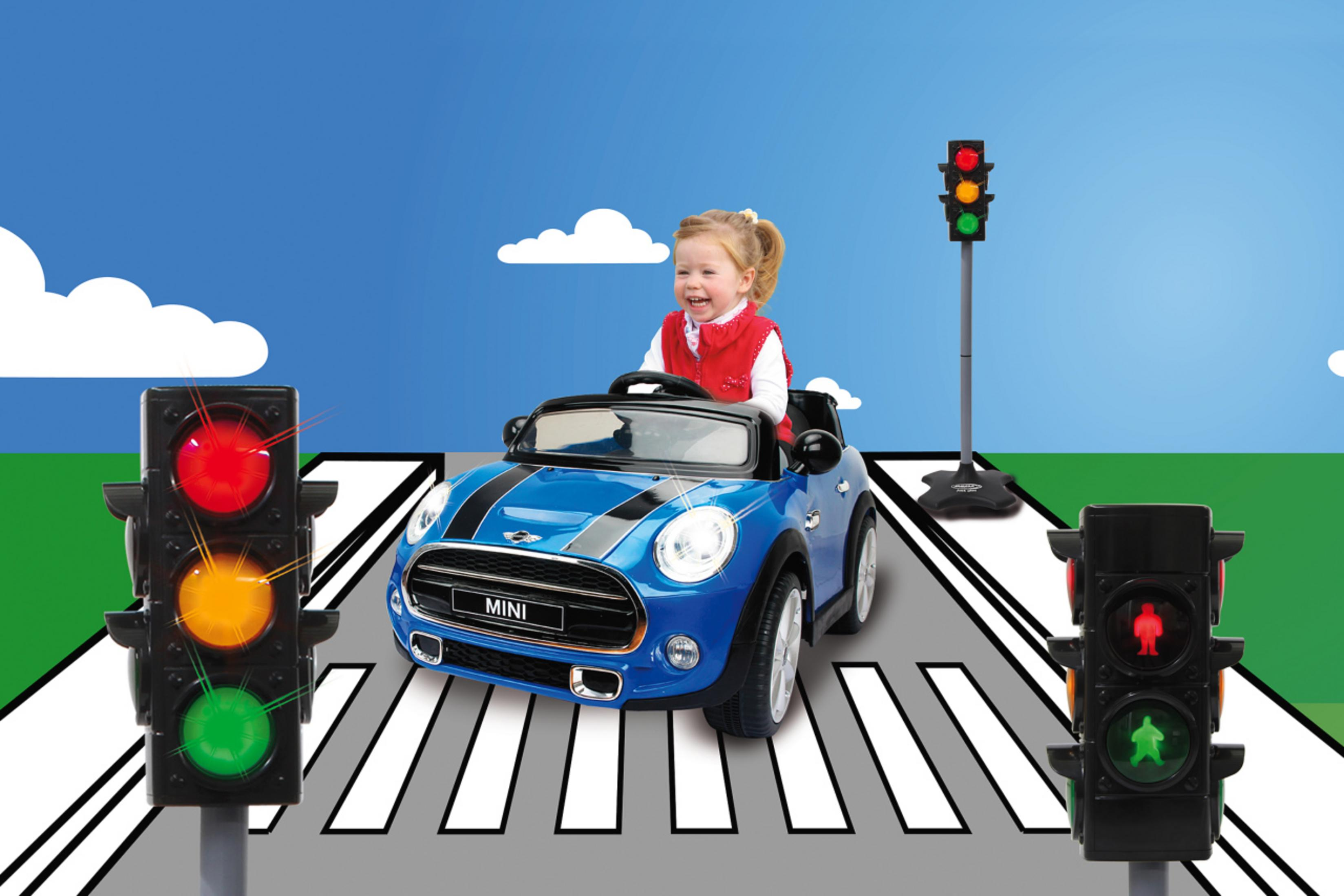 Dziecko w niebieskim samochodziku na pasach. Po obu stronach sygnalizatory świetlne.