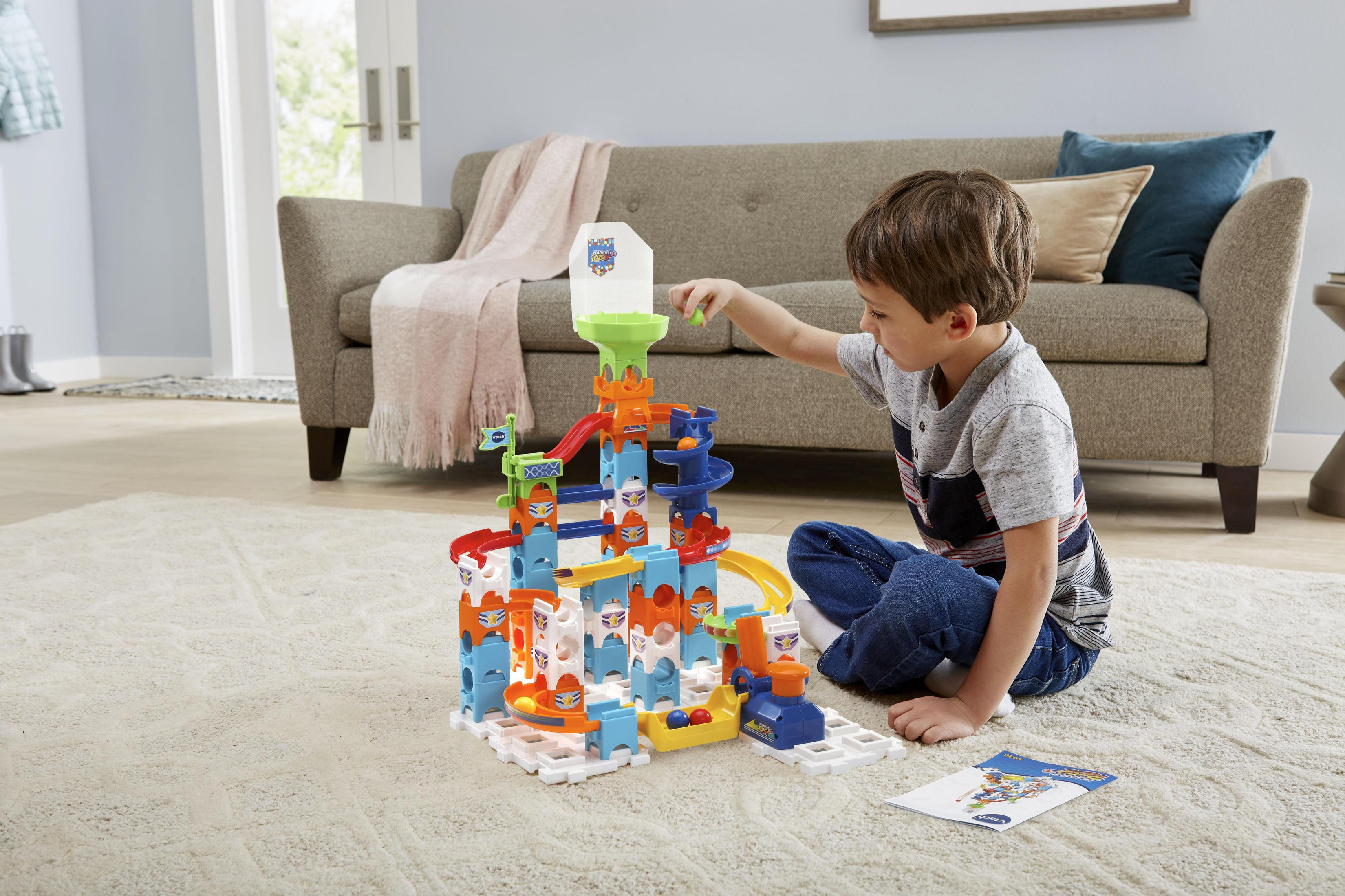 Ein Junge spielt mit einem bunten Spielzeug-Set auf einem Teppich. Das Spielzeug hat Kugeln, Rampen und einen Turm.
