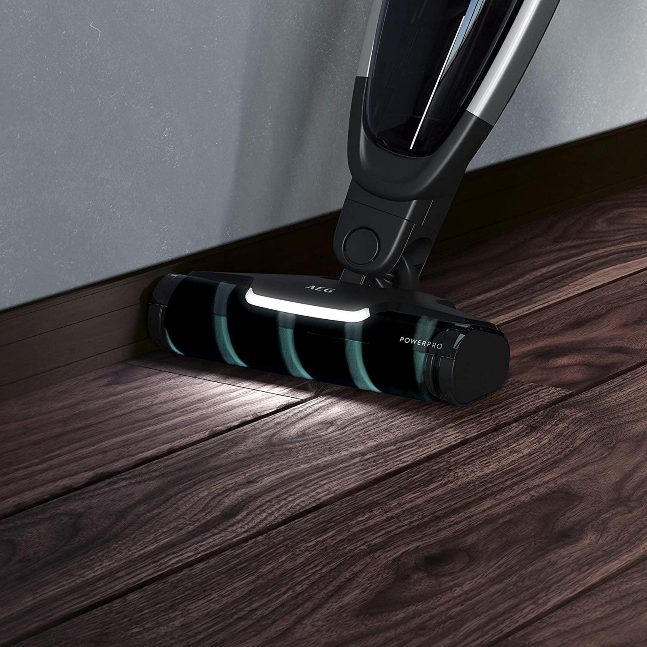Cabezal de aspiradora negra en suelo de madera, resaltado por la luz.