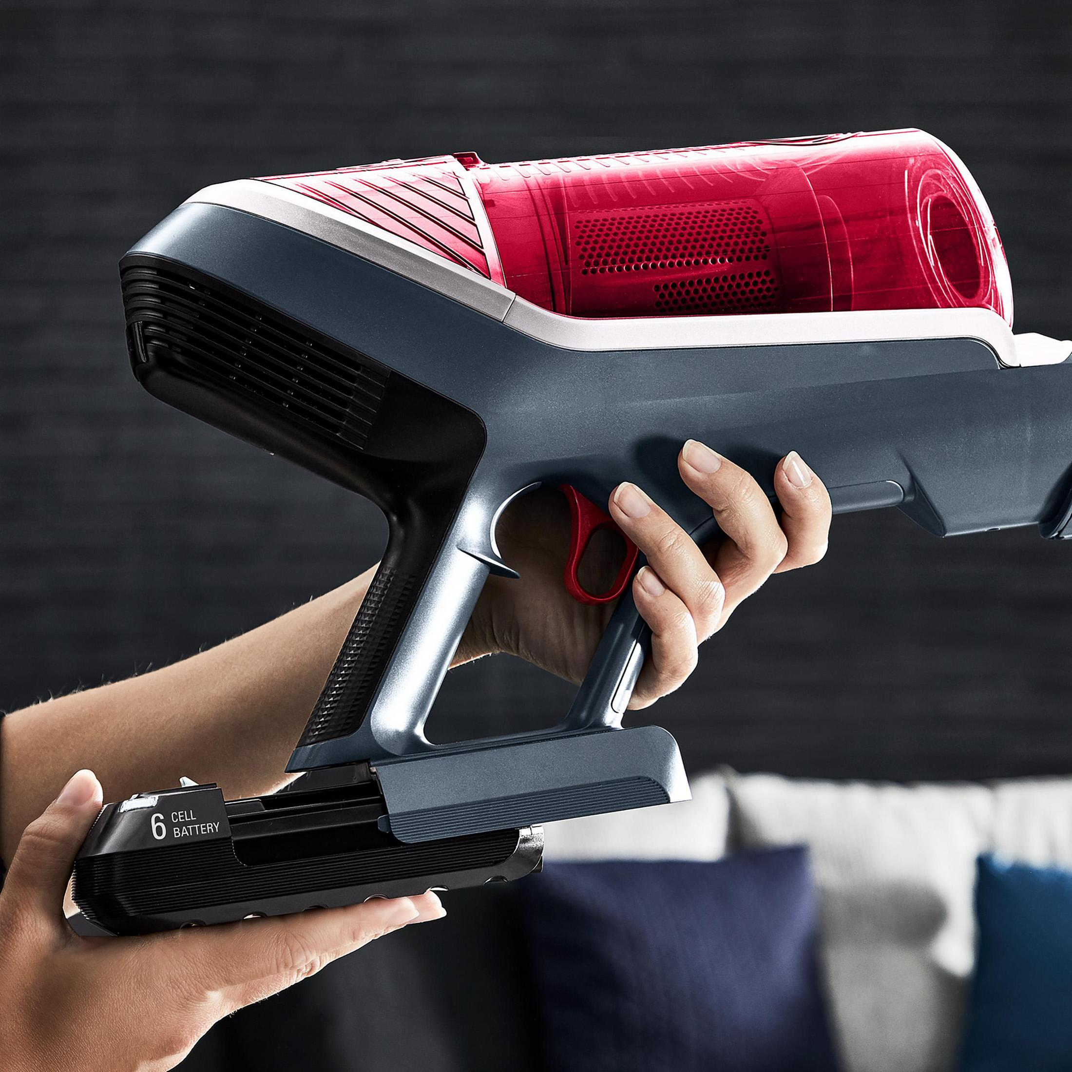 Osoba trzyma bezprzewodowy odkurzacz. Góra jest czerwona i szara, z dołączoną baterią.