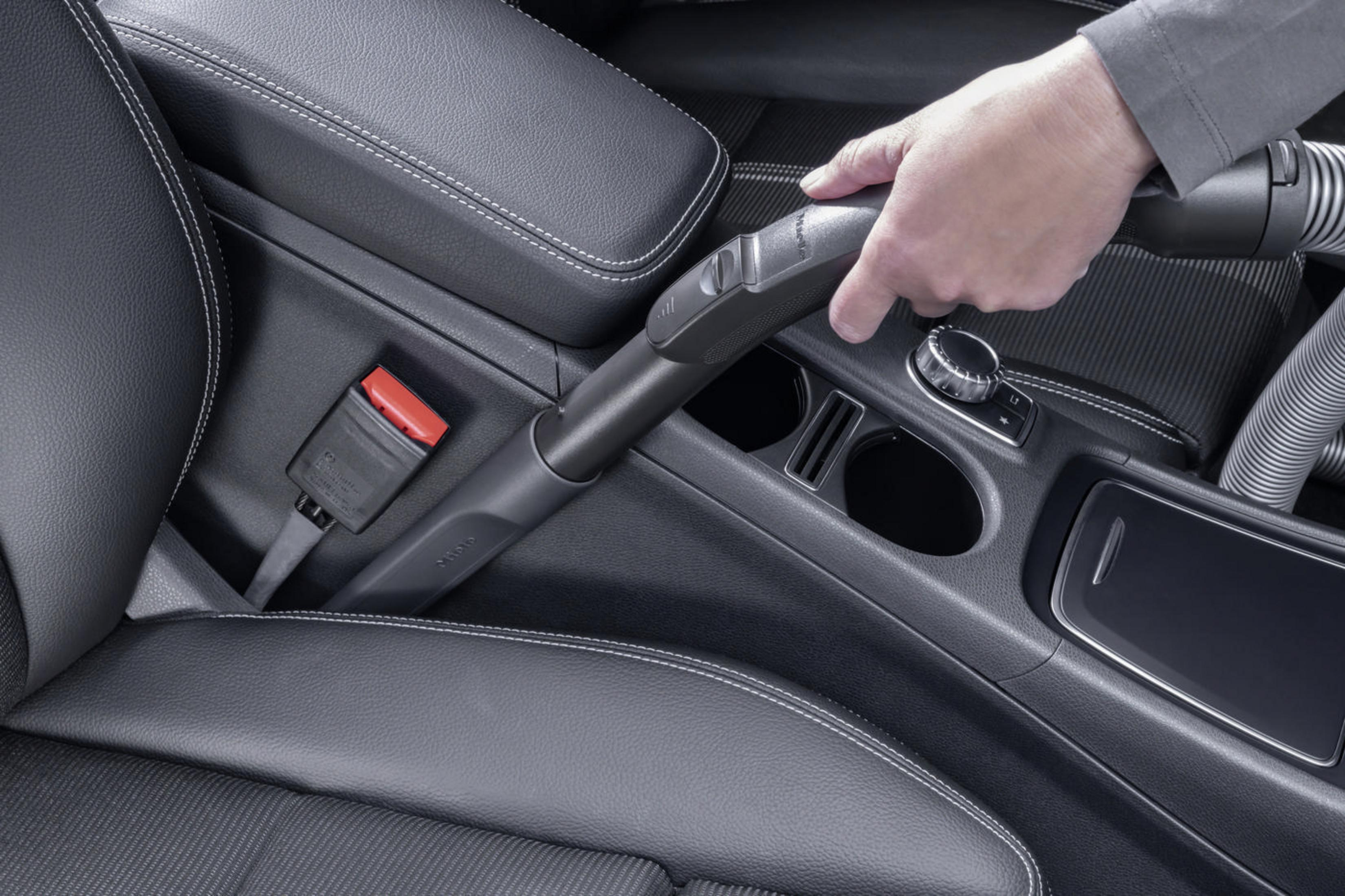 Hand saugt Auto-Innenraum. Staubsauger ist schwarz, Innenraum ist schwarz und grau.