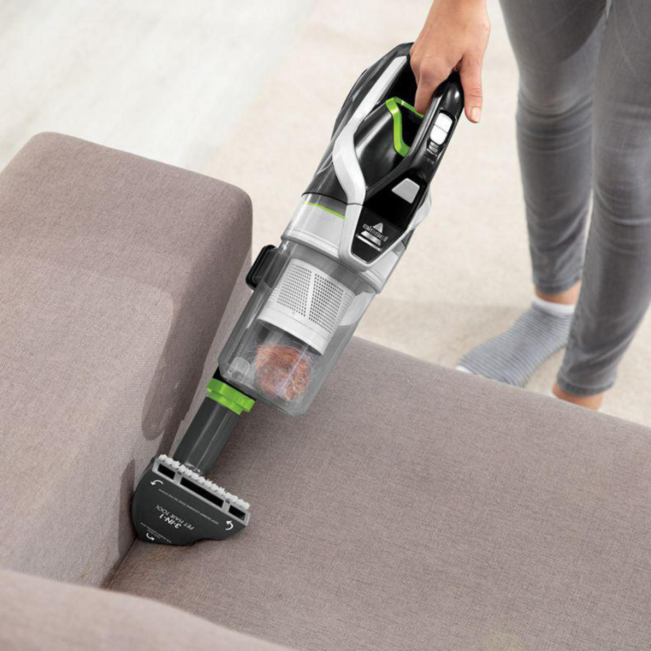 Eine Frau benutzt einen Bissell-Staubsauger auf einem Sofa. Der Staubsauger ist schwarz und grün.