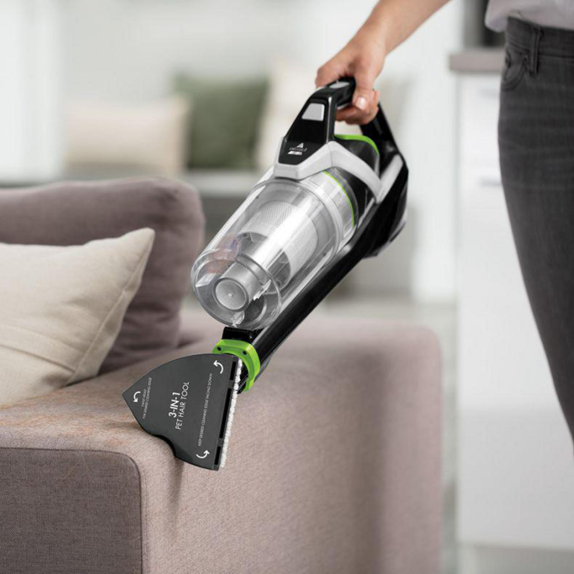 Eine Person hält einen kabellosen Staubsauger über ein Sofa. Der Staubsauger ist schwarz, grün und silber.