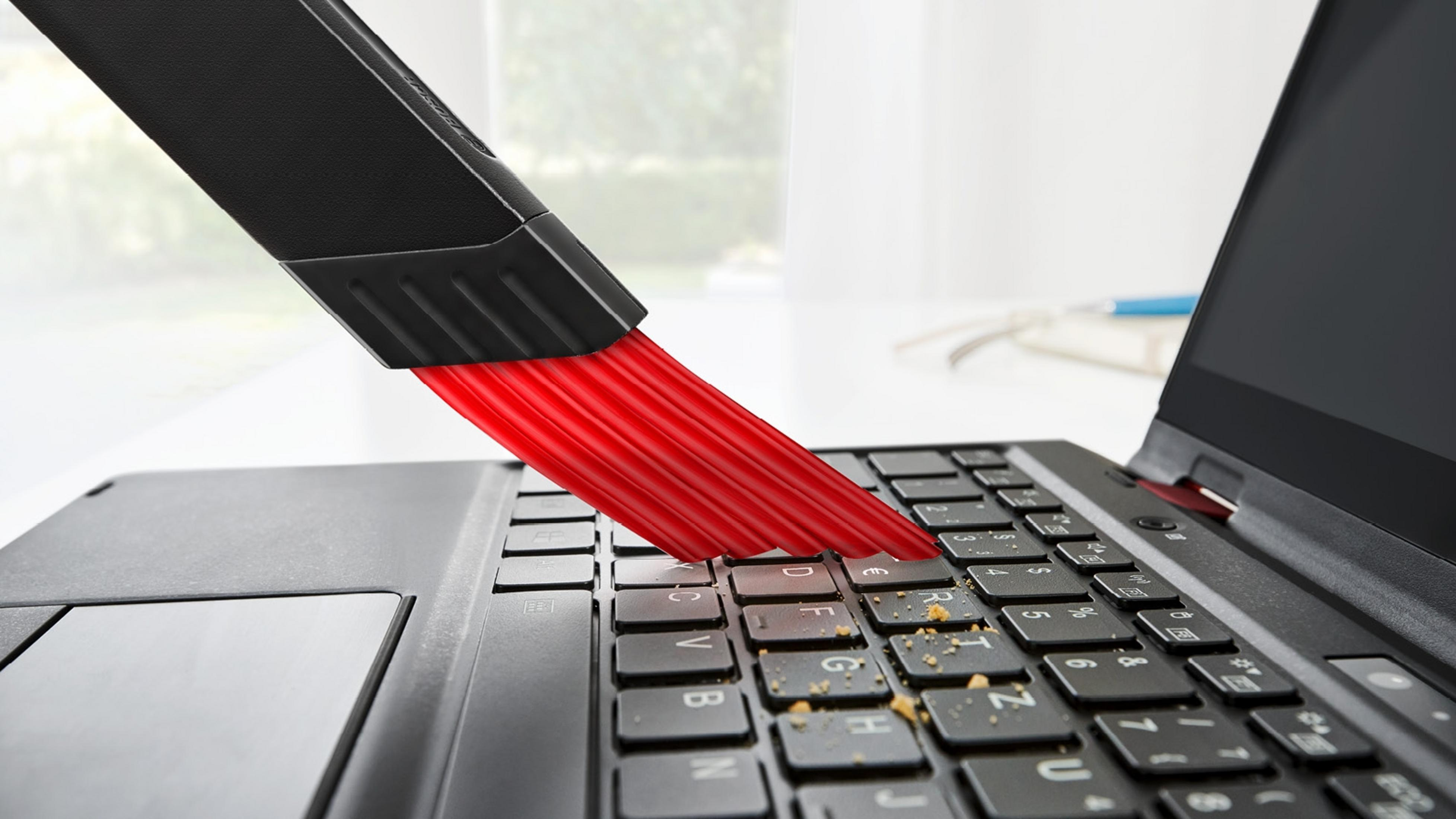 Un cepillo negro limpia un teclado de portátil, eliminando polvo y residuos.