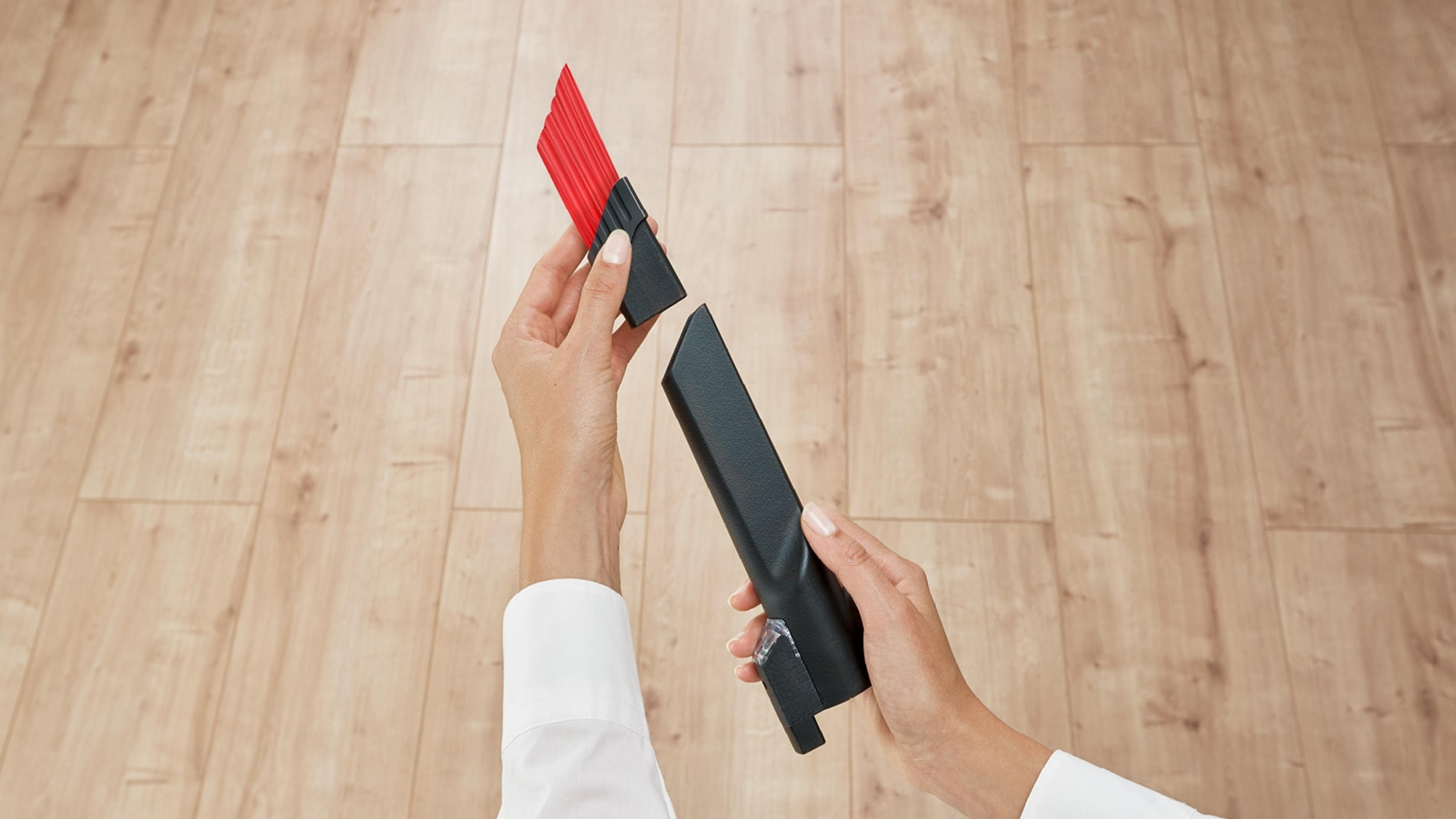 Manos ensamblando un accesorio de aspiradora. Fondo de piso de madera, camisa blanca.