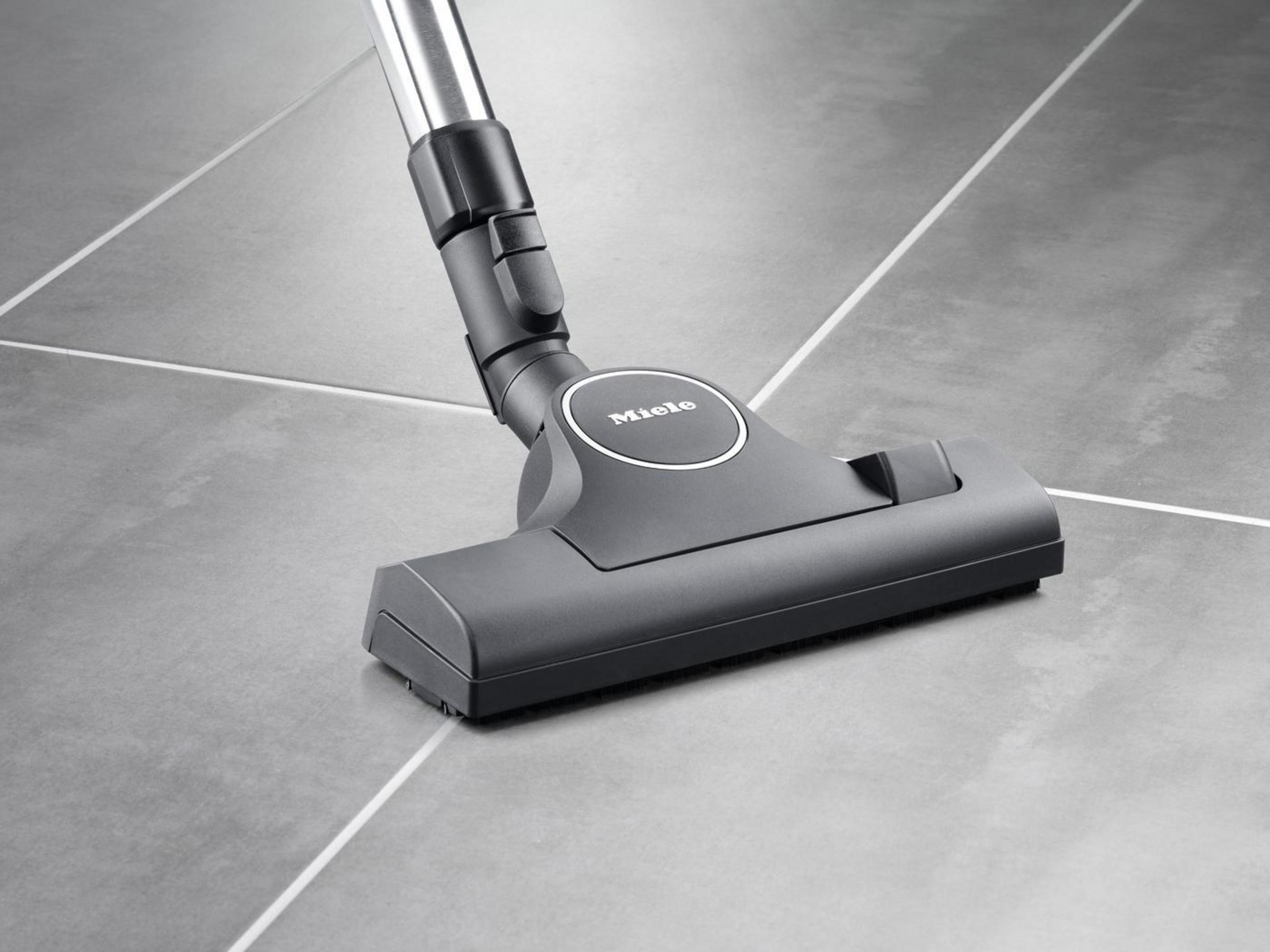 Miele Staubsaugerkopf auf grauem Fliesenboden. Dunkelgrau, Miele Logo sichtbar.