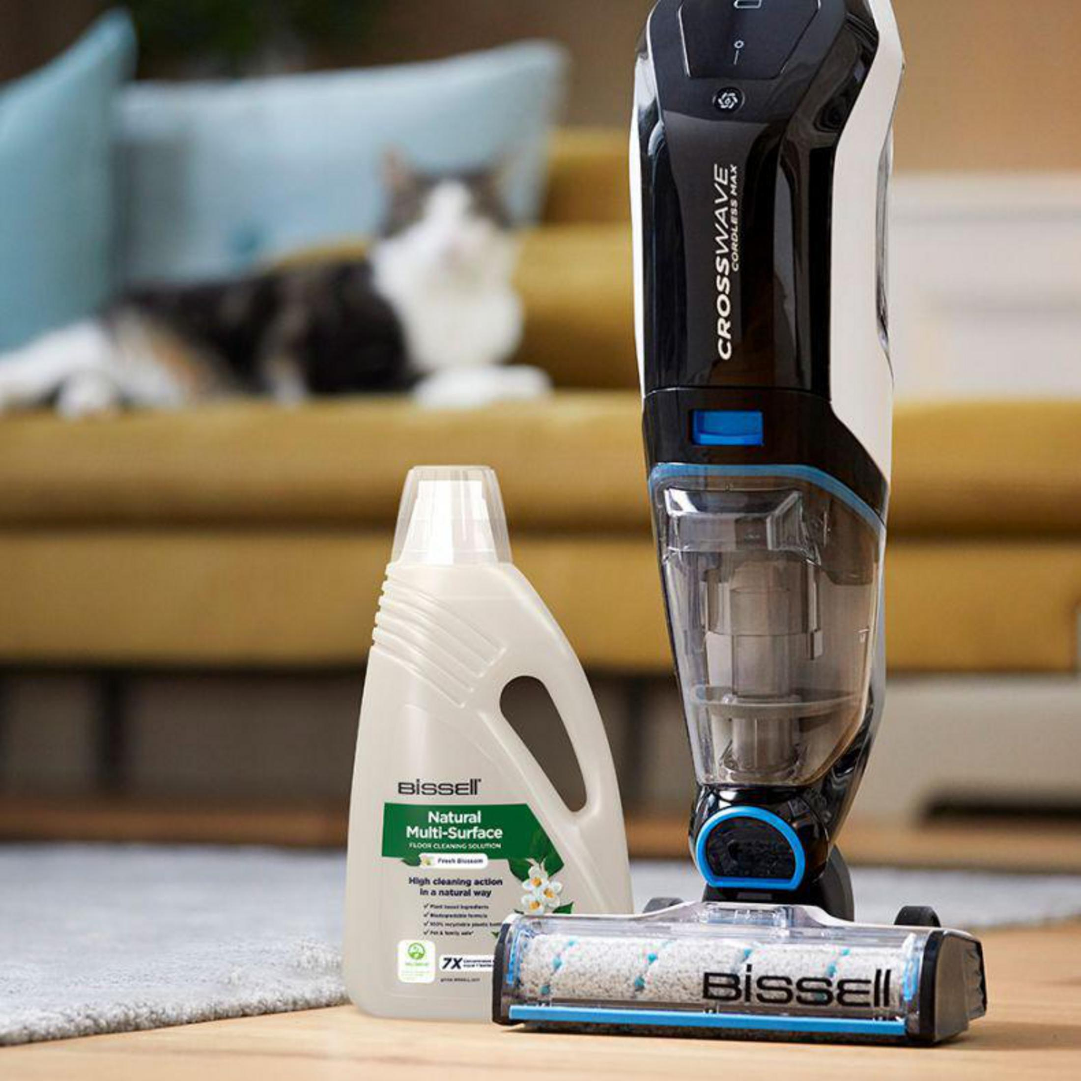 Un flacone di detergente e soluzione per la pulizia Bissell Crosswave è su un pavimento in legno. Un gatto è sullo sfondo.