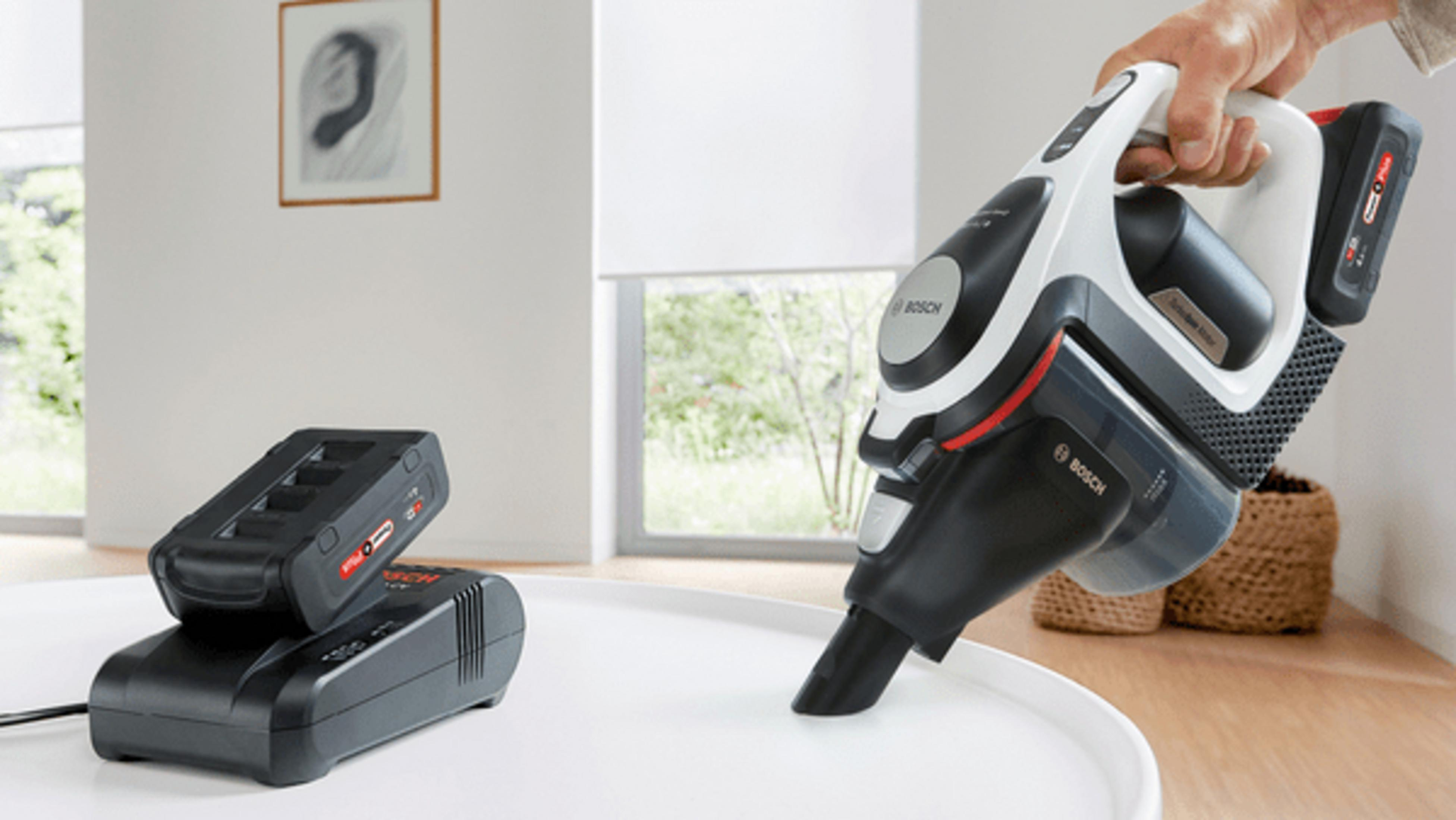 Osoba trzymająca odkurzacz ręczny Bosch, obok ładowarka.