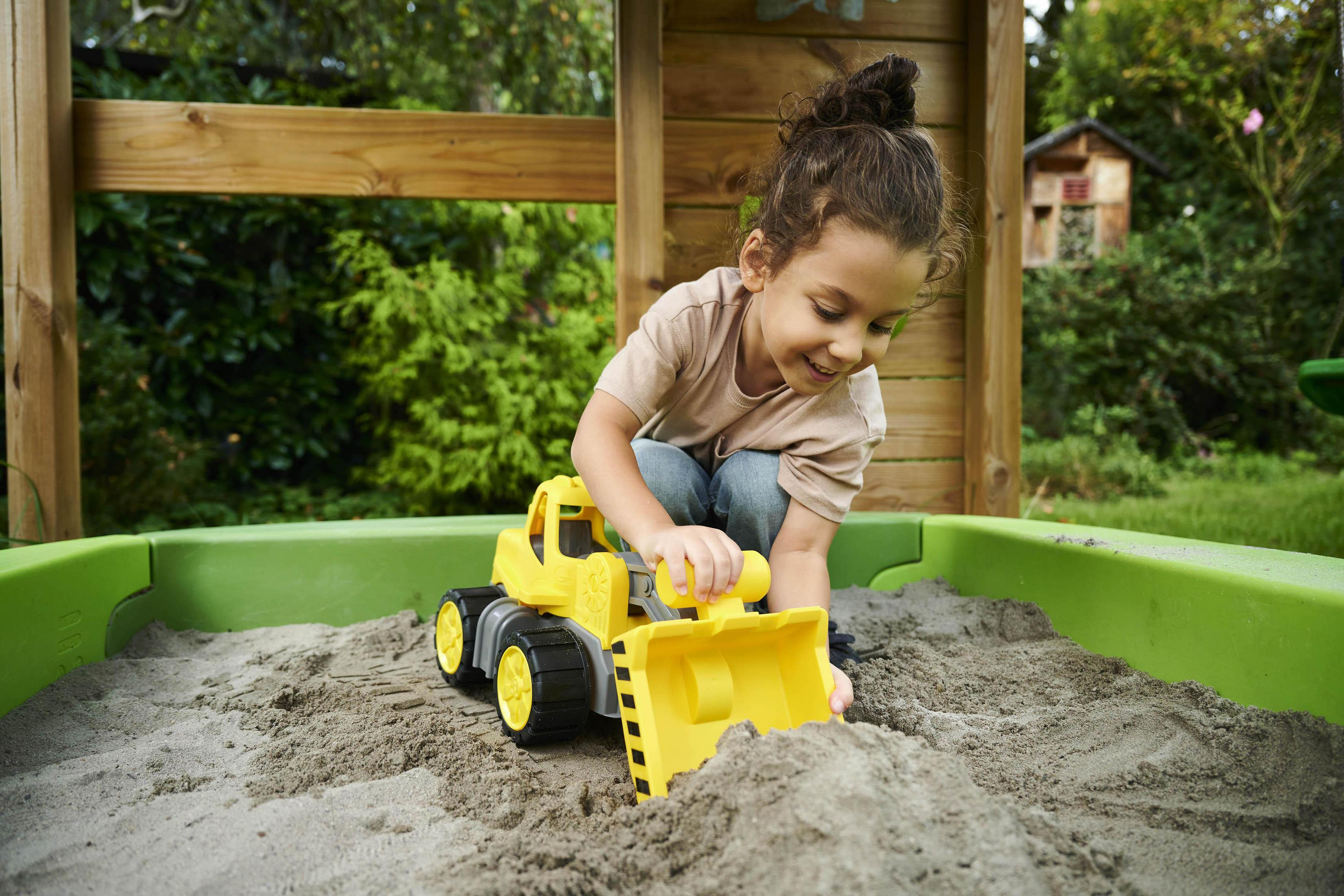 Dziecko bawi się żółtą zabawką-ciężarówką w piaskownicy.