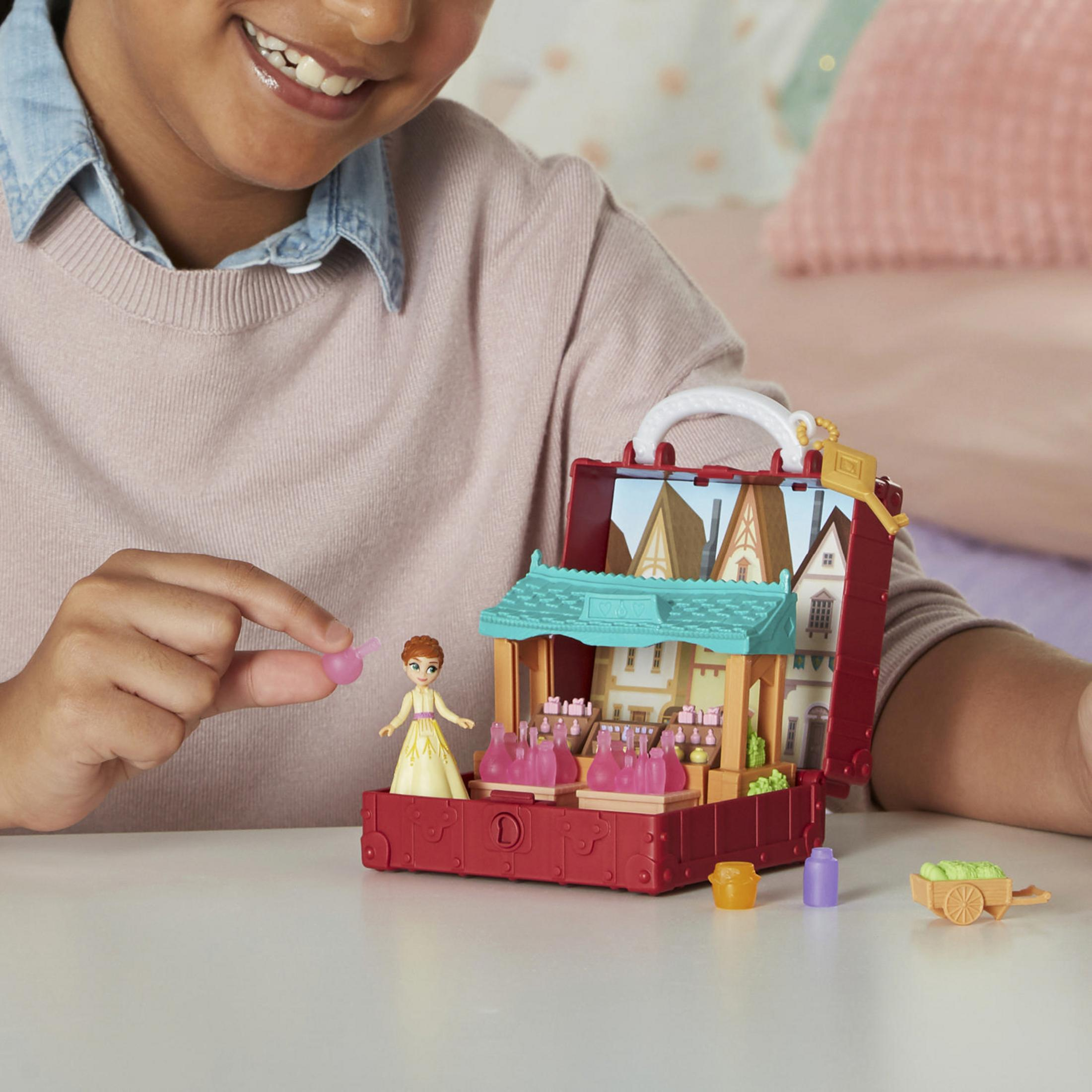 Dziewczynka bawi się zestawem zabawek Kraina Lodu. Zestaw to miniaturowa wioska w walizce.