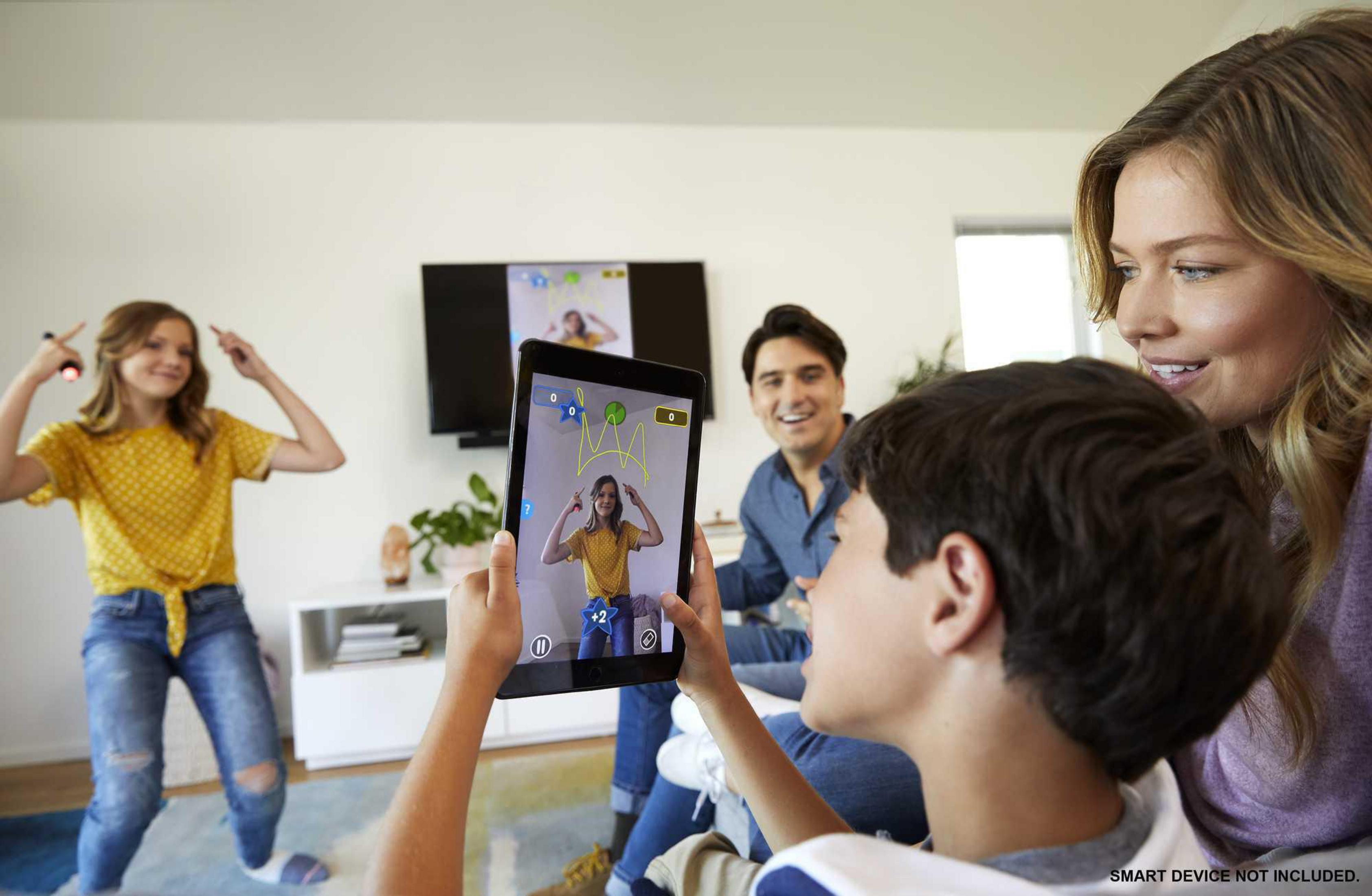 Eine Familie spielt ein Spiel auf einem Tablet. Ein Mädchen tanzt. Das Tablet zeigt eine Zeichnung.