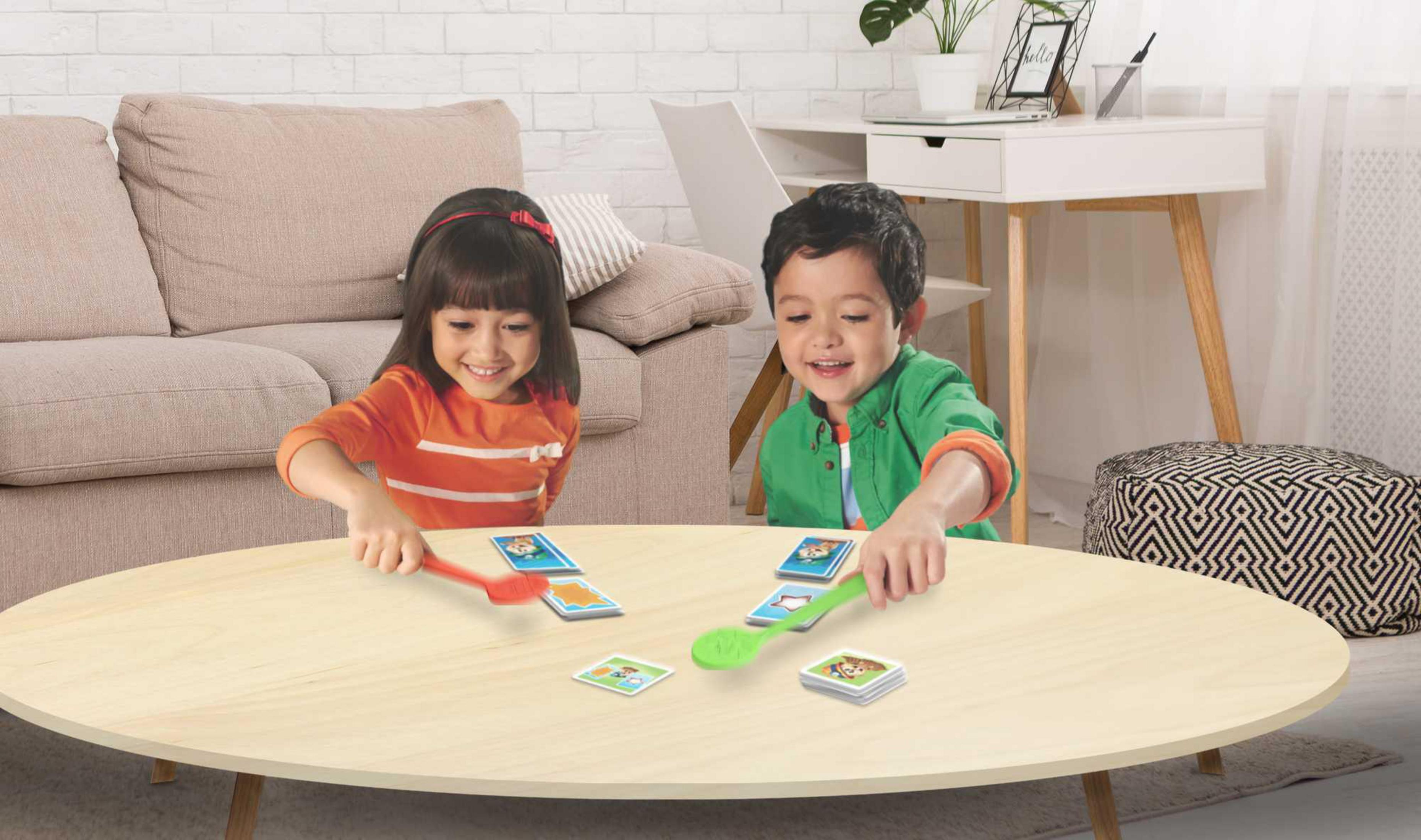 Zwei Kinder spielen ein Kartenspiel. Sie sitzen an einem Holztisch mit Karten und Löffeln.