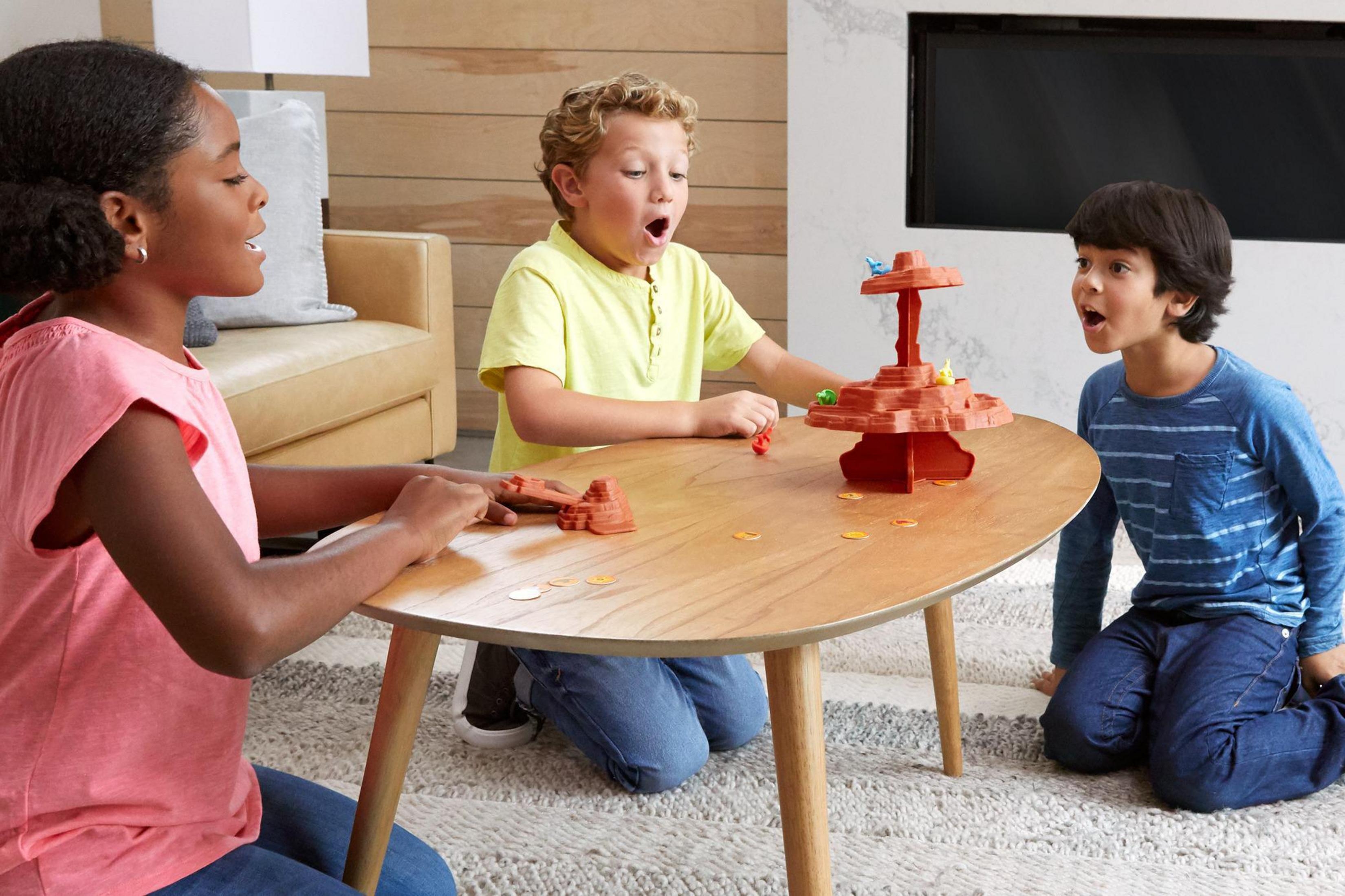 Drei Kinder spielen ein Brettspiel auf einem Holztisch. Ein rotes Spiel in der Mitte.