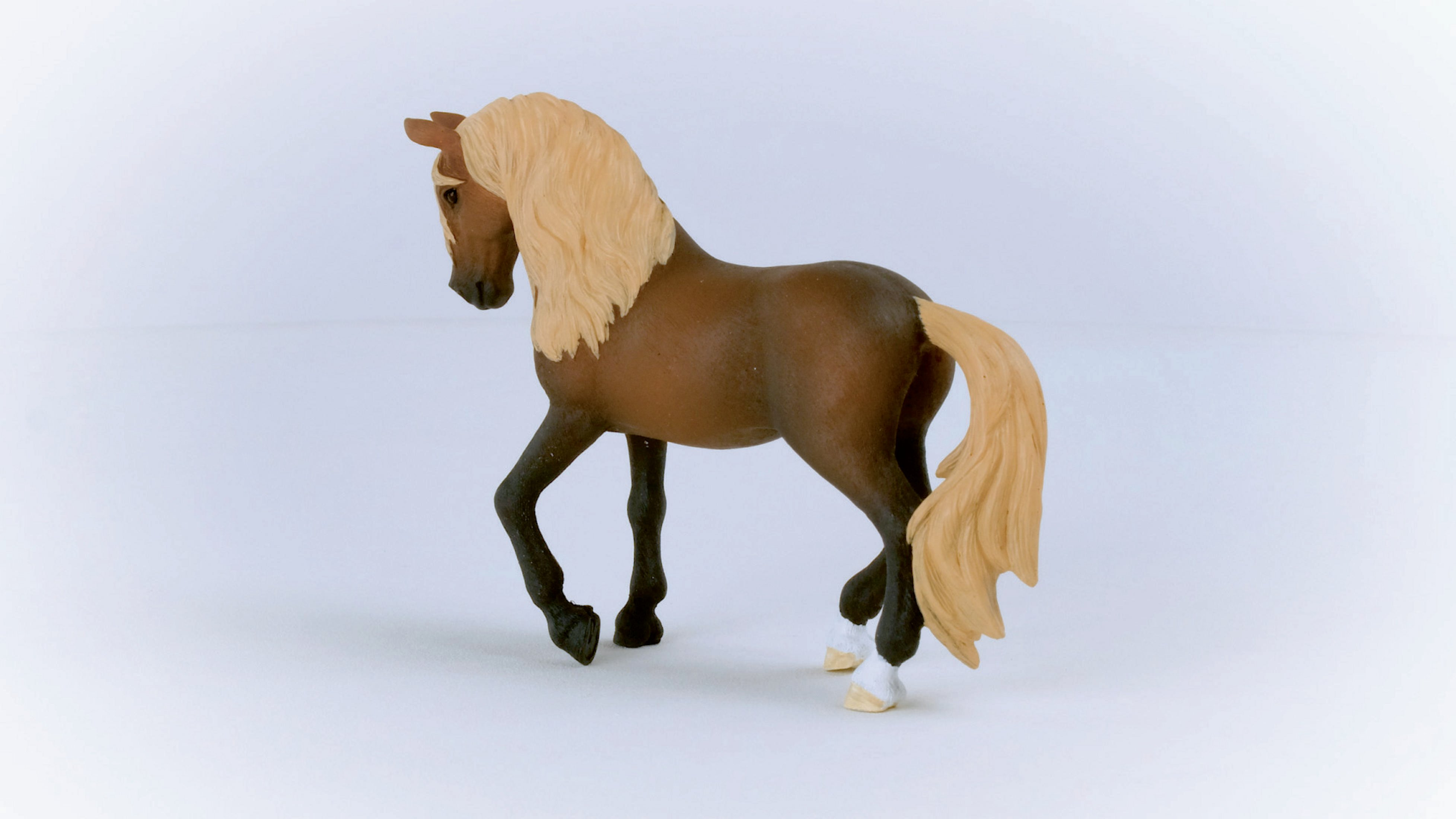 Brązowa zabawka konia z jasną grzywą i ogonem na białym tle. Koń patrzy w lewo.