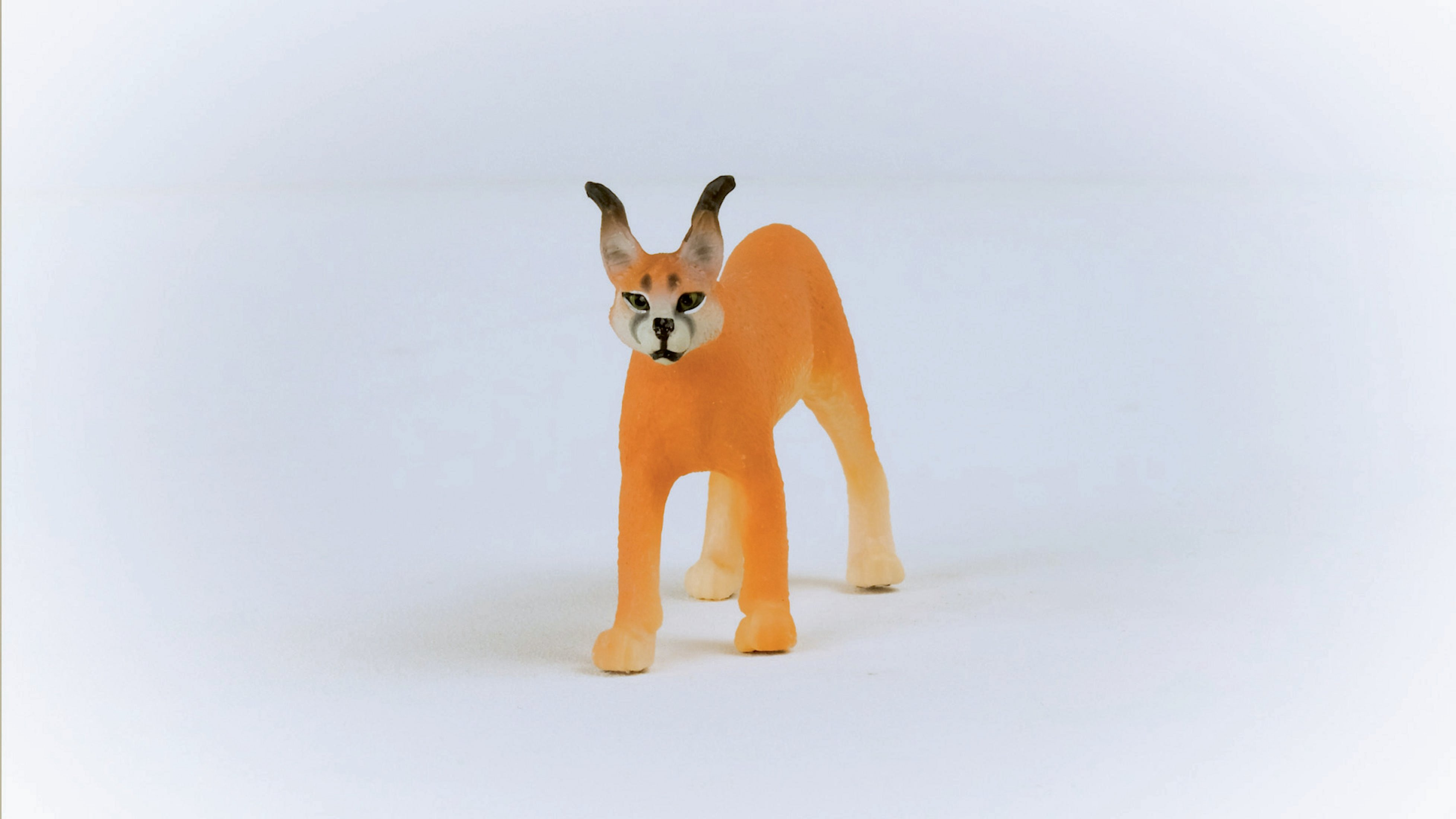 Pomarańczowa figurka zabawki karakala na białym tle, stojąca i patrząca w przód.