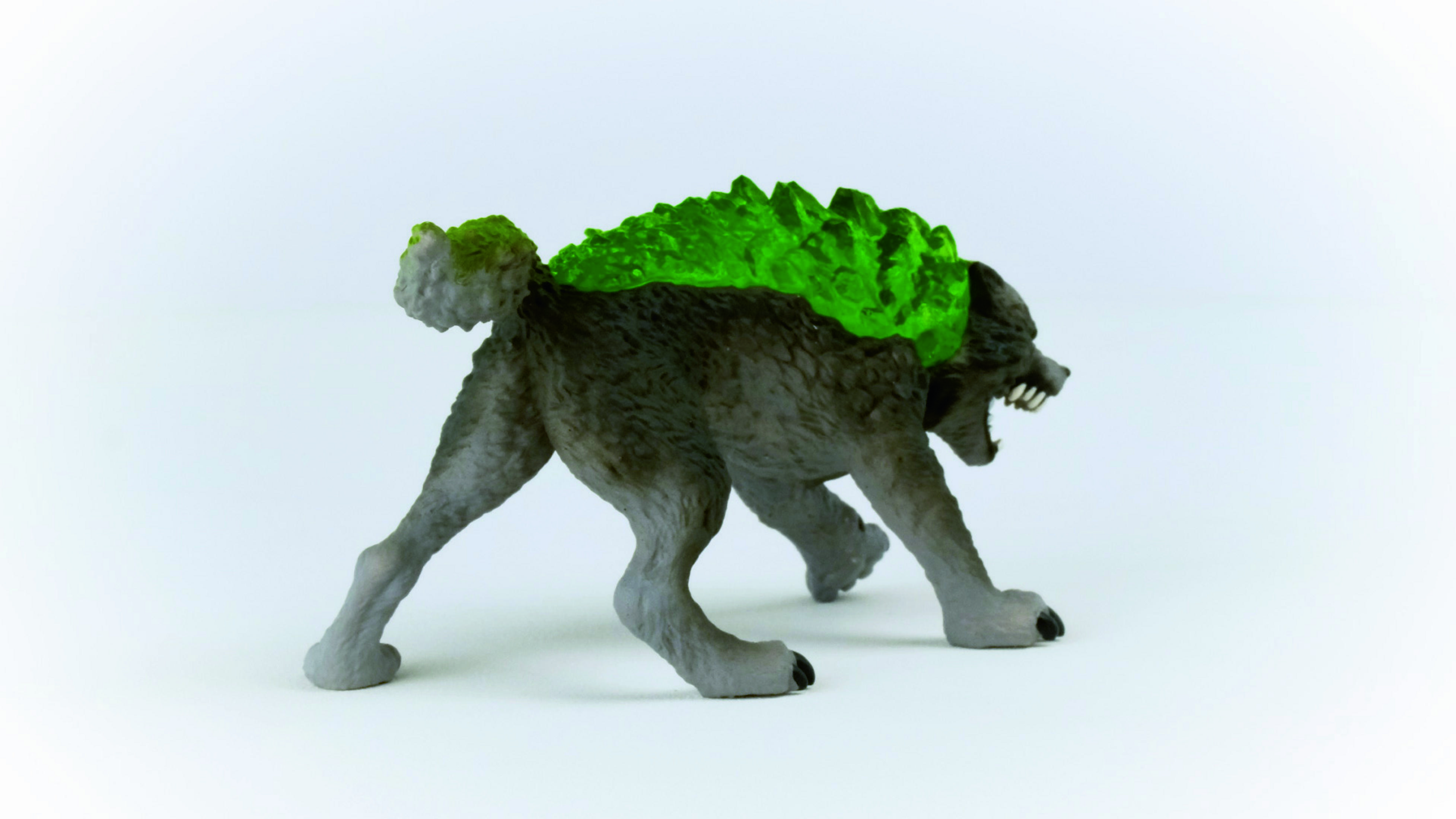 Un giocattolo grigio simile a un lupo con la schiena verde e appuntita, su sfondo bianco, di profilo.