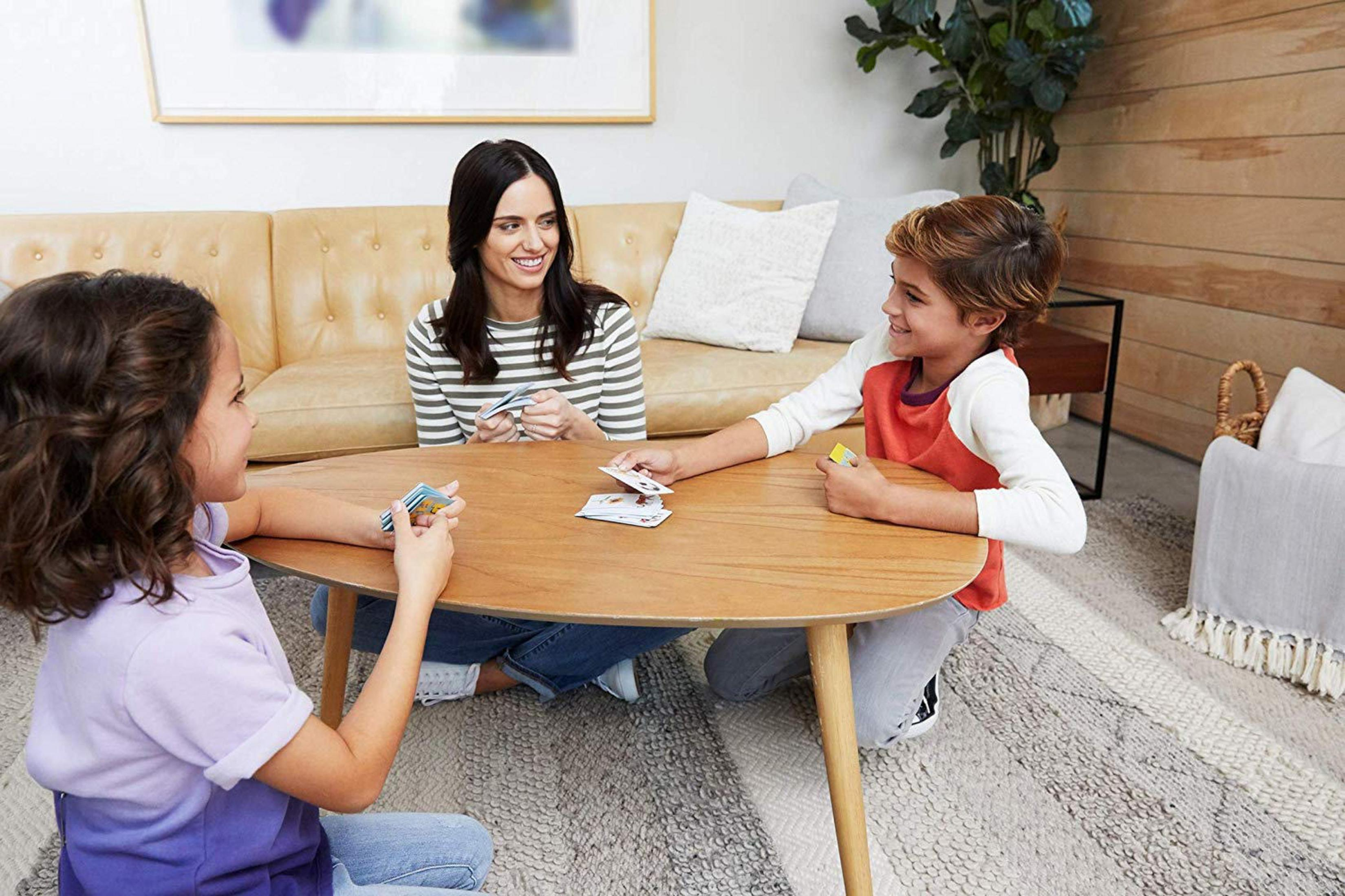 Eine Familie spielt ein Kartenspiel um einen Holztisch in einem Wohnzimmer.