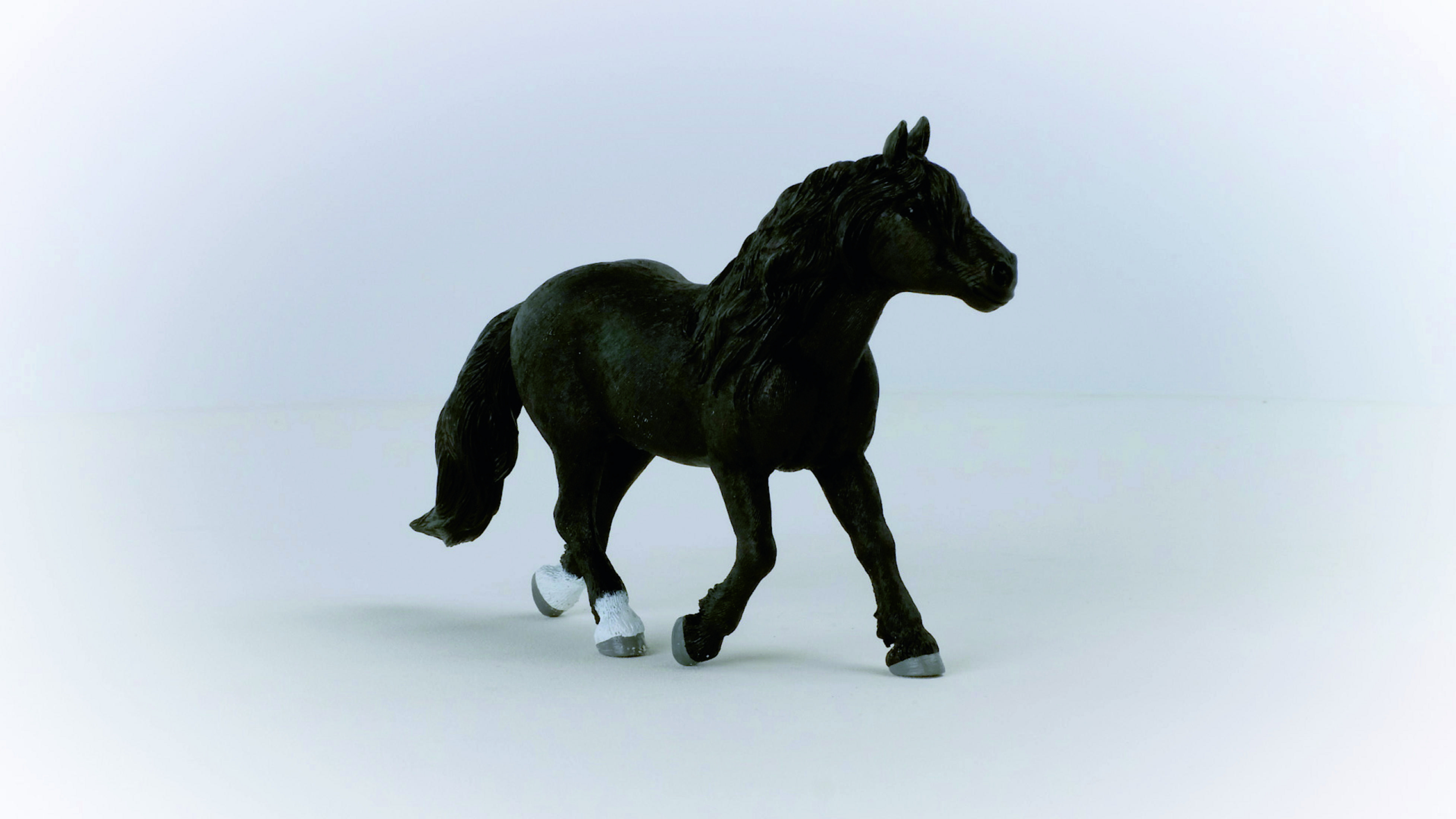 Czarny zabawkowy koń w pozycji biegu, na białym tle.