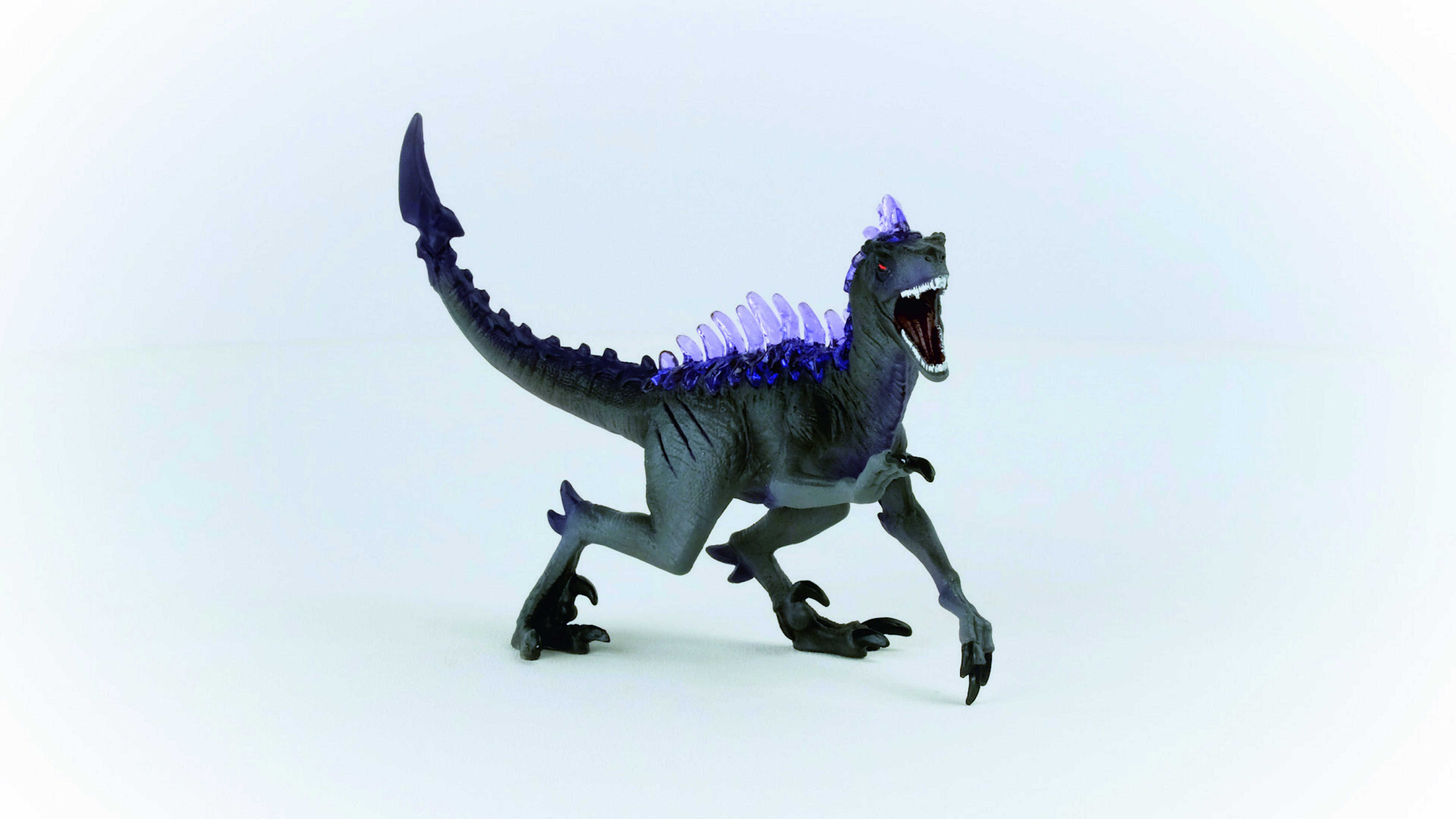 Ein graues Dinosaurier-Spielzeug mit lila Stacheln und offenem Mund, auf einer weißen Oberfläche posiert.