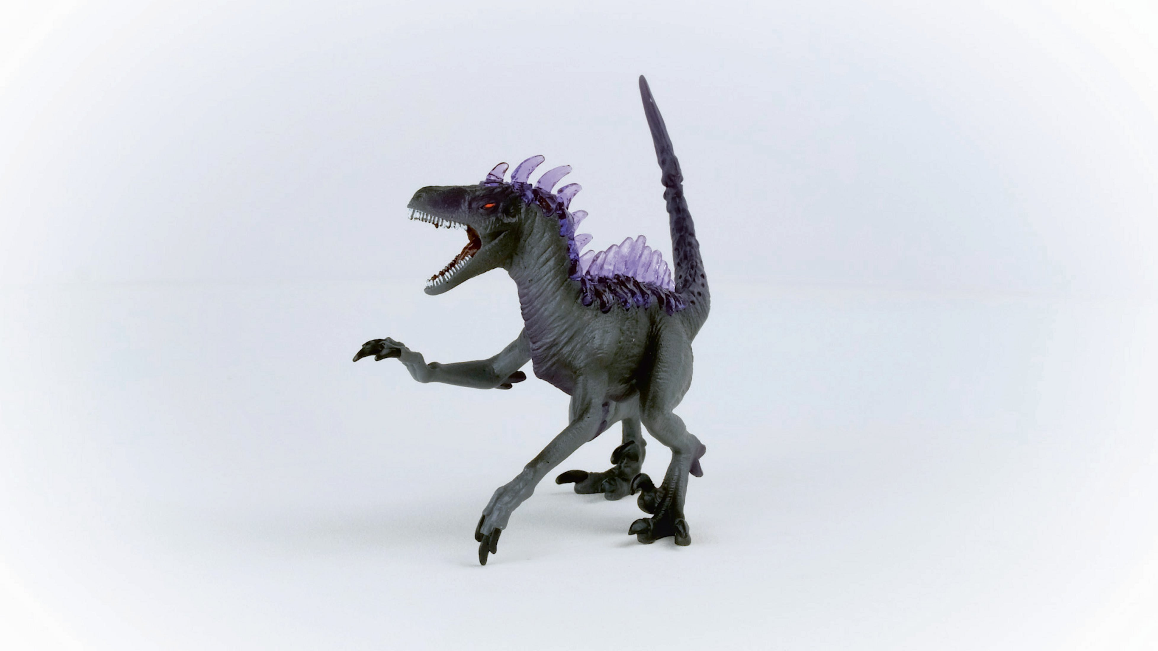 Ein graues Dinosaurierspielzeug mit lila Stacheln auf Rücken und Kopf, auf weißem Hintergrund.