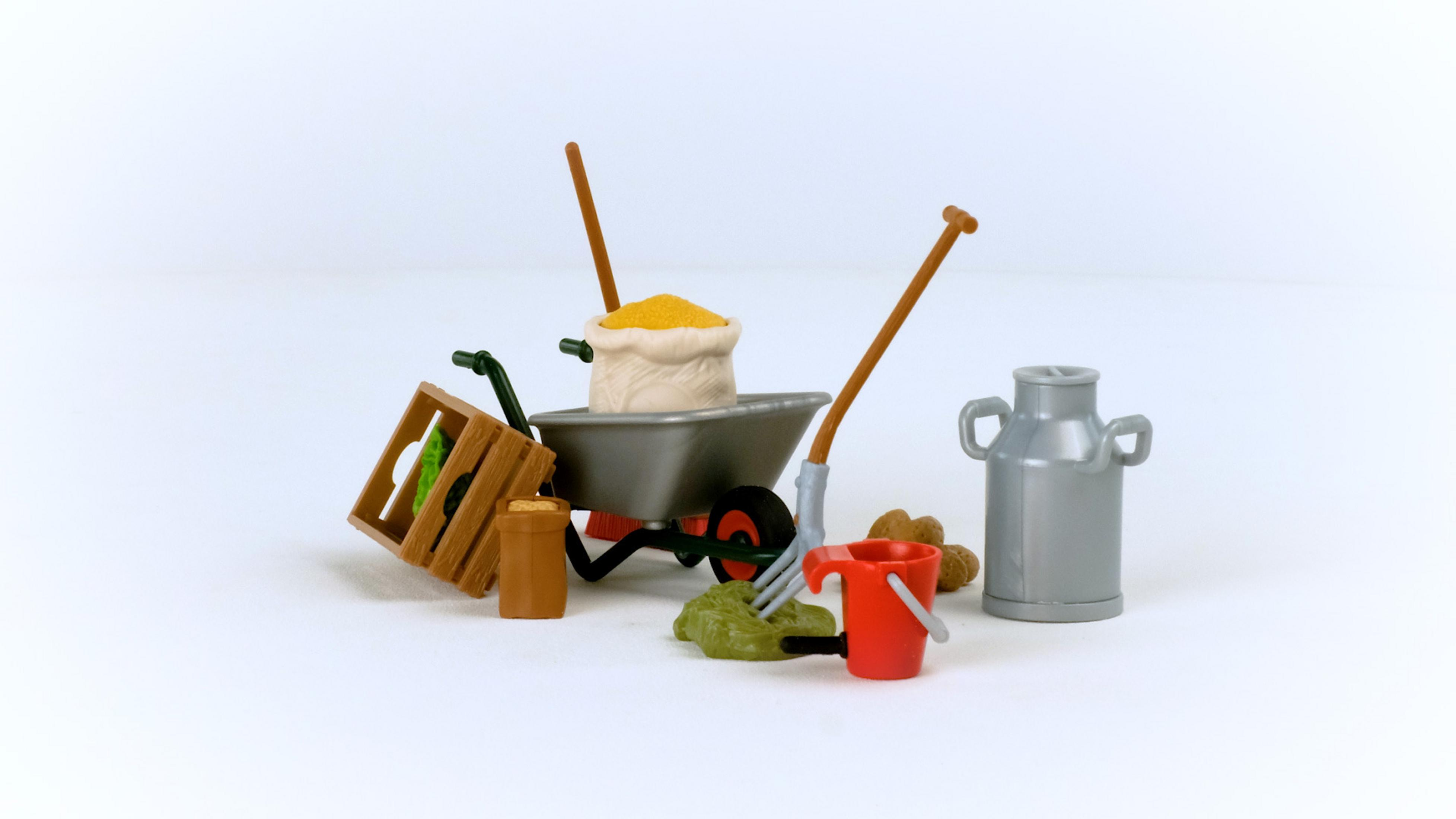 Bauernhofwerkzeuge auf weißer Oberfläche. Enthält Schubkarre, Eimer, Gabel und Milchkännchen.