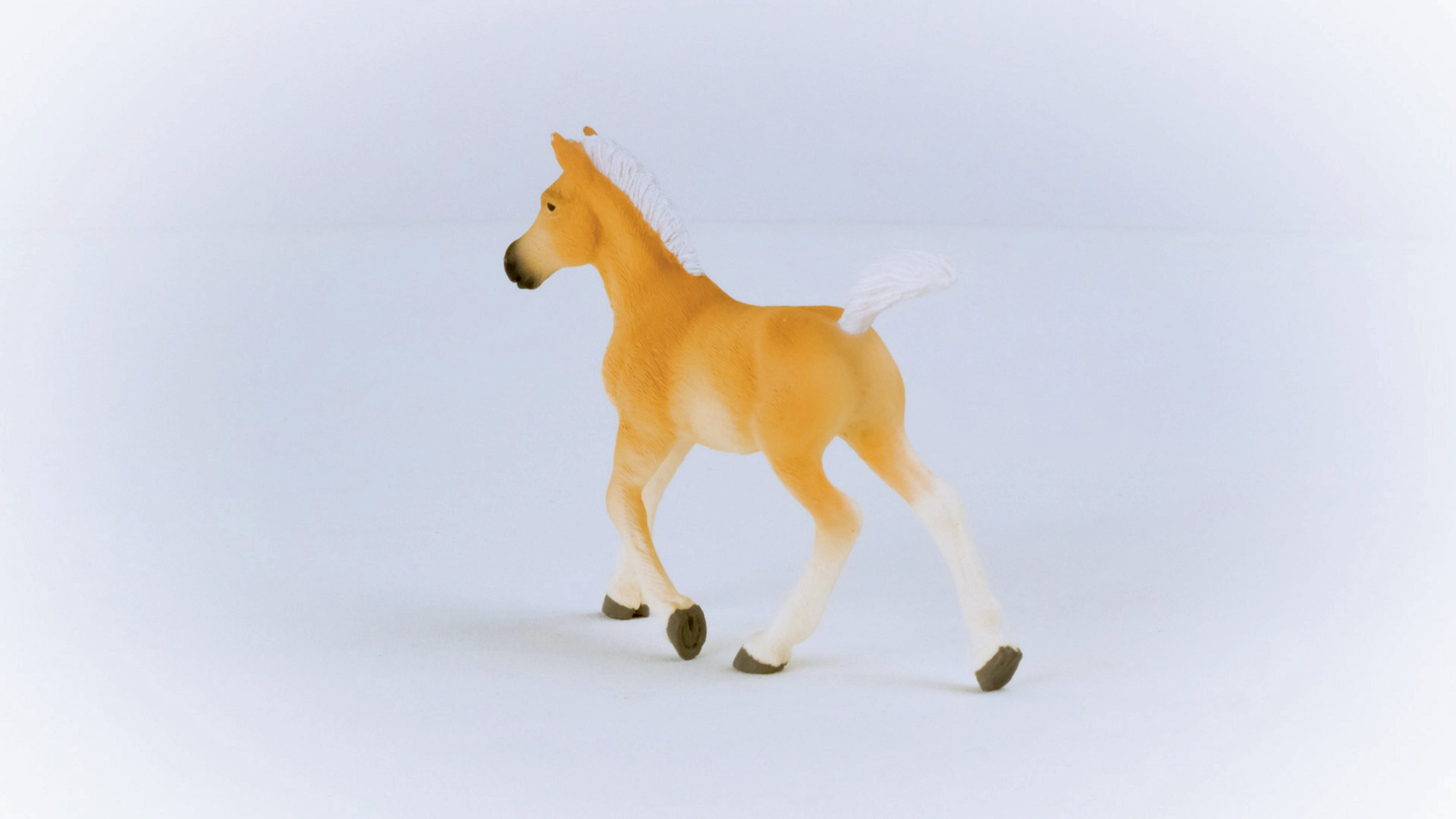Mały, brązowy zabawkowy źrebię. Stoi na białej powierzchni, tyłem do widza.