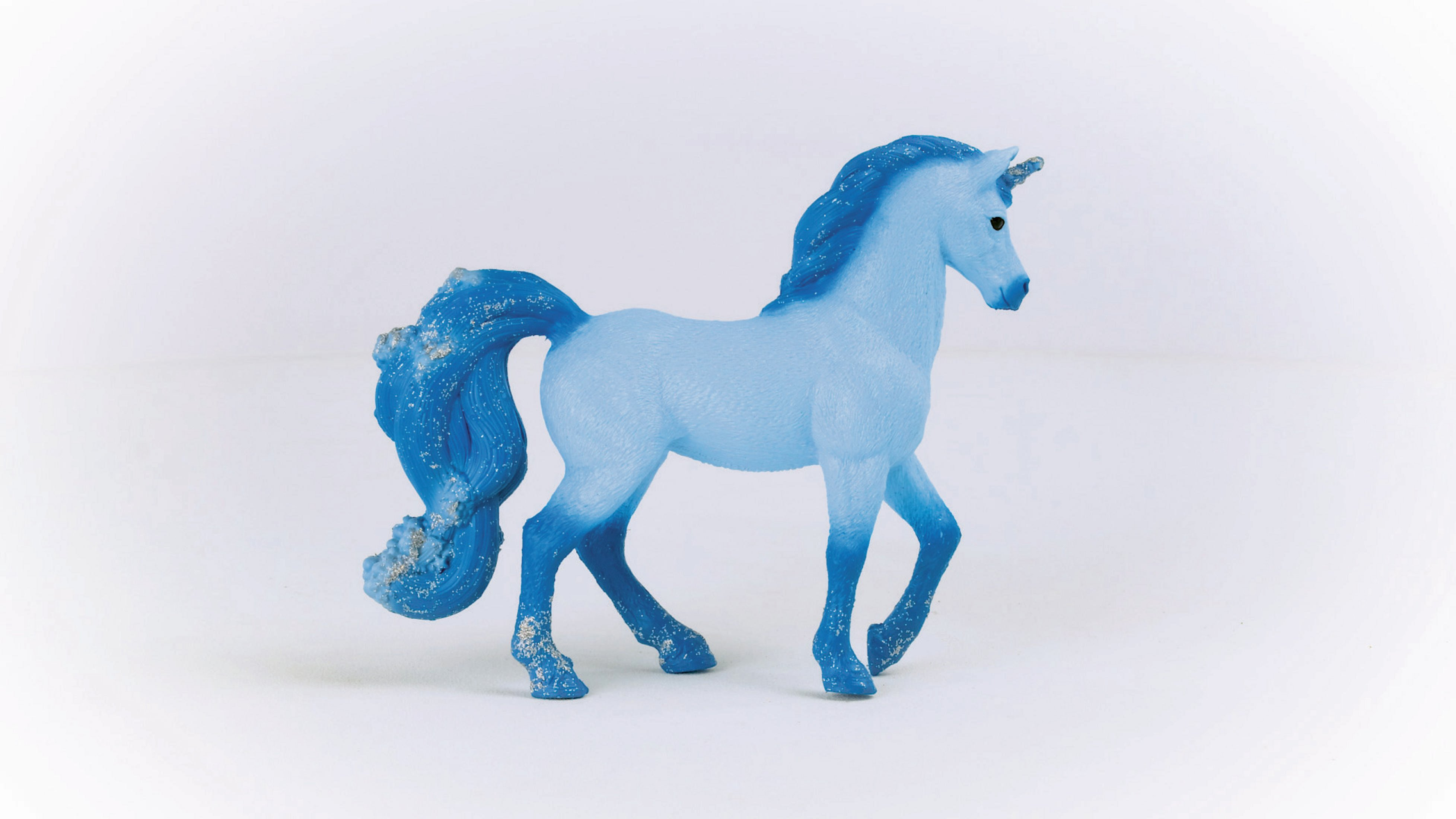 Niebieska zabawka jednorożca na białym tle, idąca w prawo.