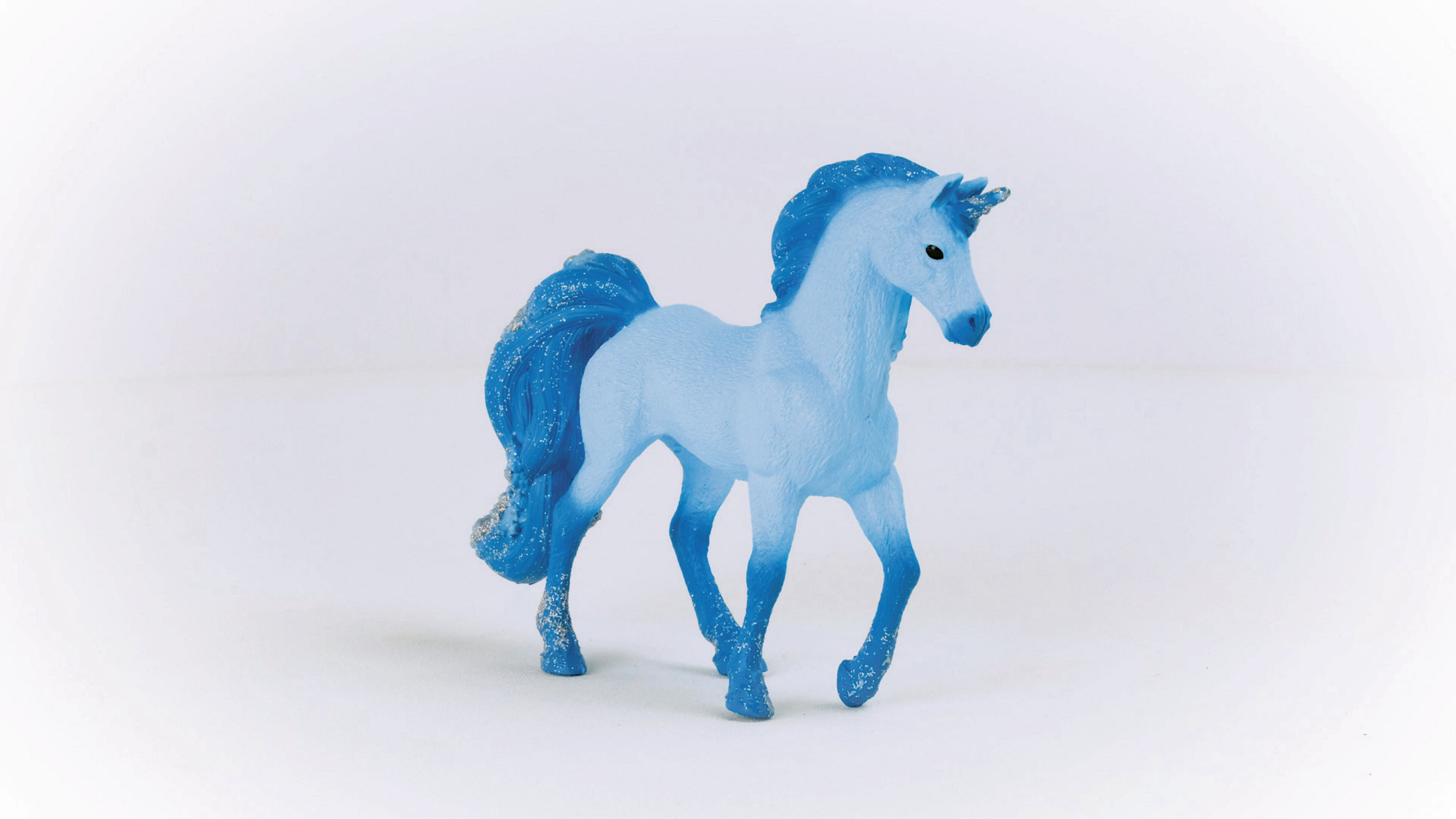 Niebieska figurka jednorożca na białej powierzchni. Grzywa i ogon mają błyszczące akcenty.