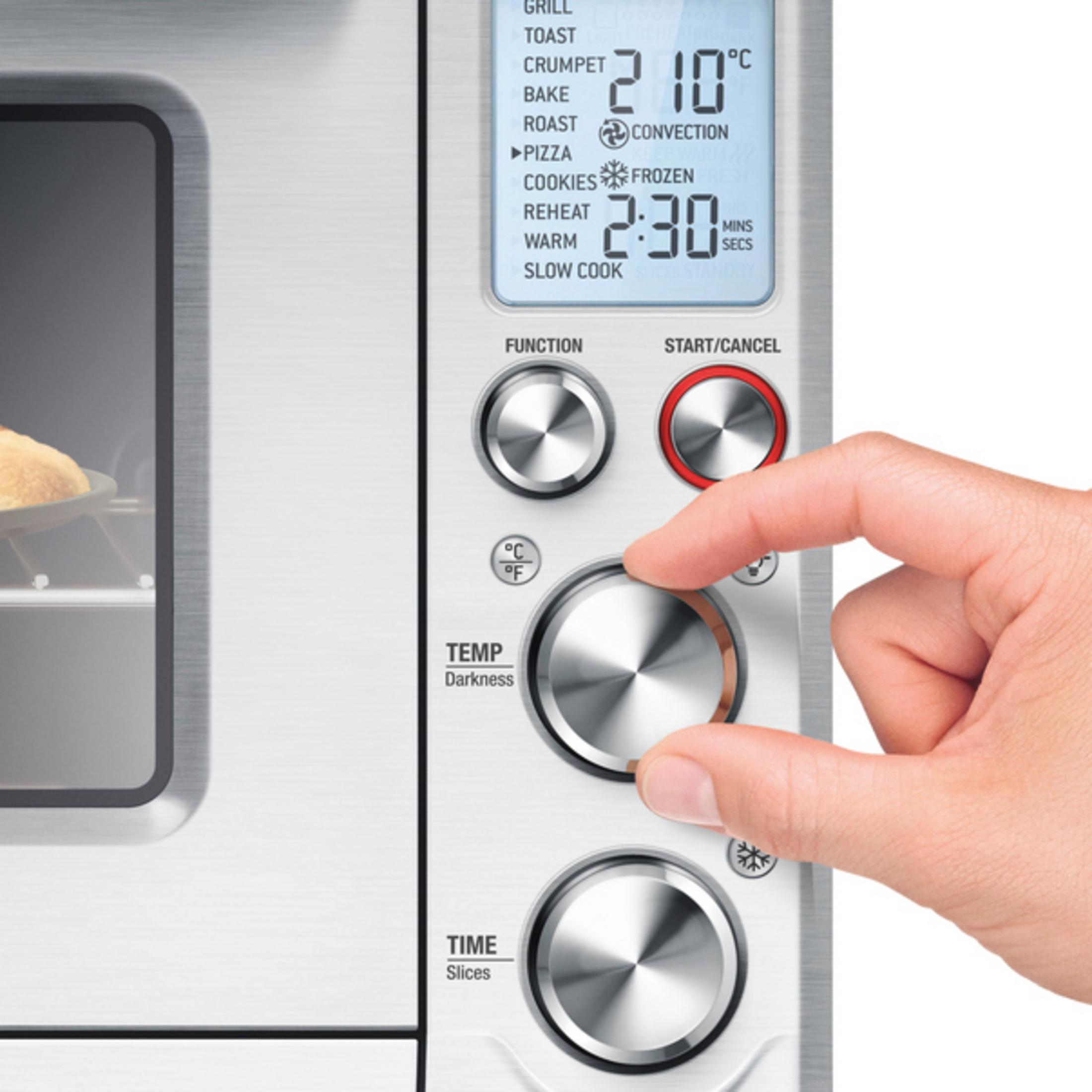 Ręka obracająca pokrętło na srebrnym piekarniku, aby ustawić temperaturę i czas.