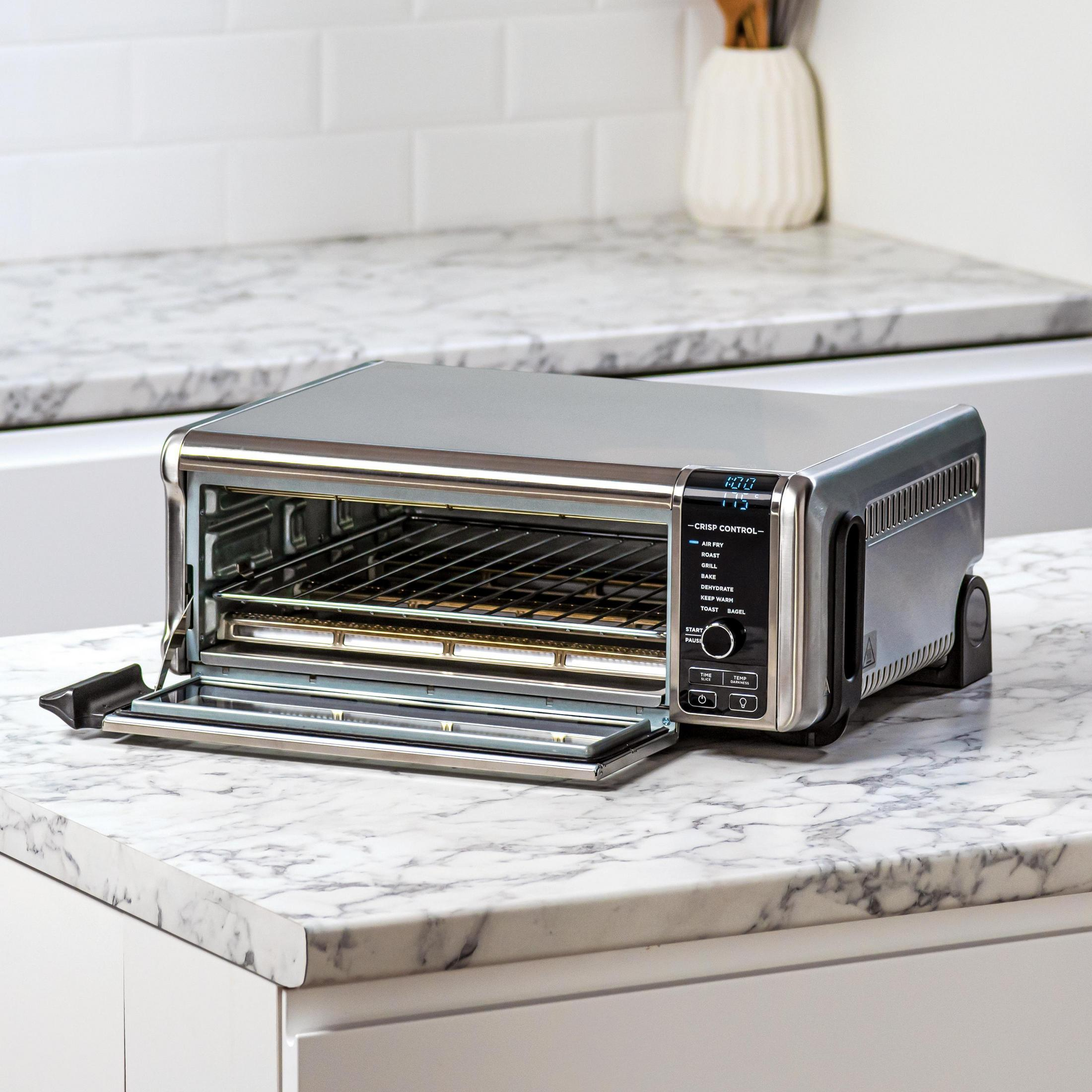 Un horno tostador plateado con la puerta abierta sobre una encimera de mármol. La pantalla muestra la hora y ajustes.