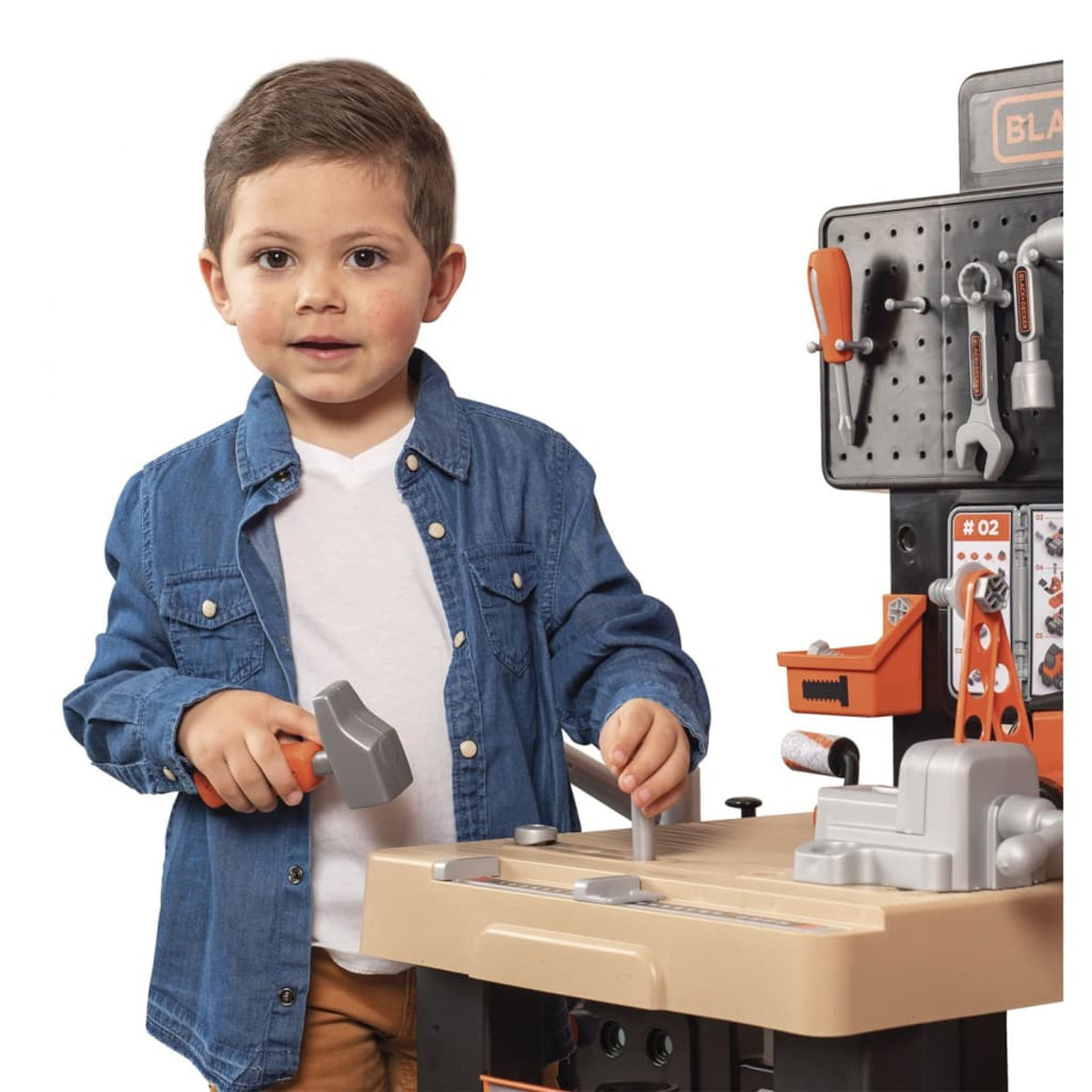Ein kleiner Junge lächelt vor einer Black & Decker Spielzeugwerkbank.