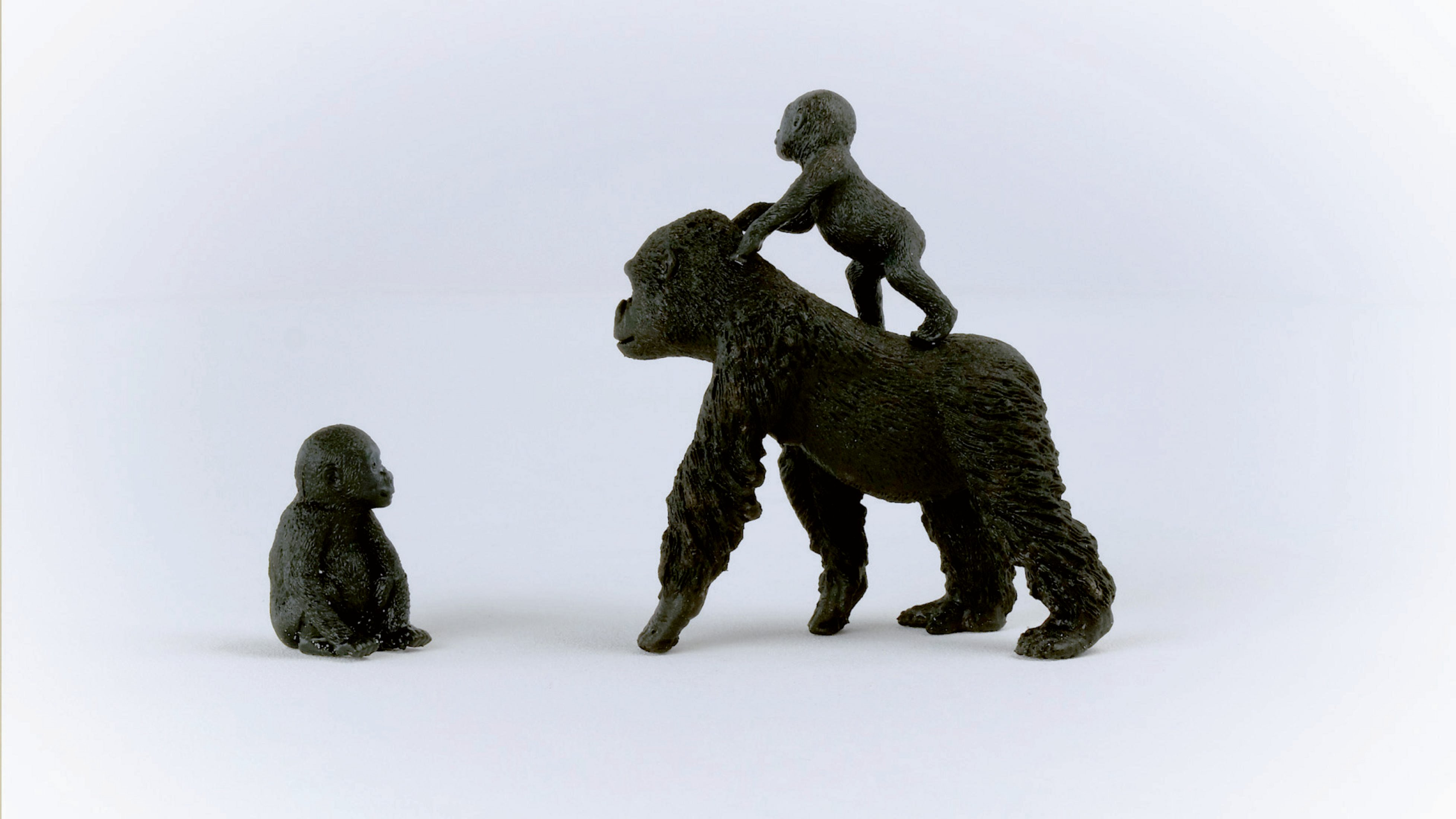 Zabawkowa goryla z dwiema małymi figurkami na grzbiecie. Jedna figurka siedzi, druga stoi.