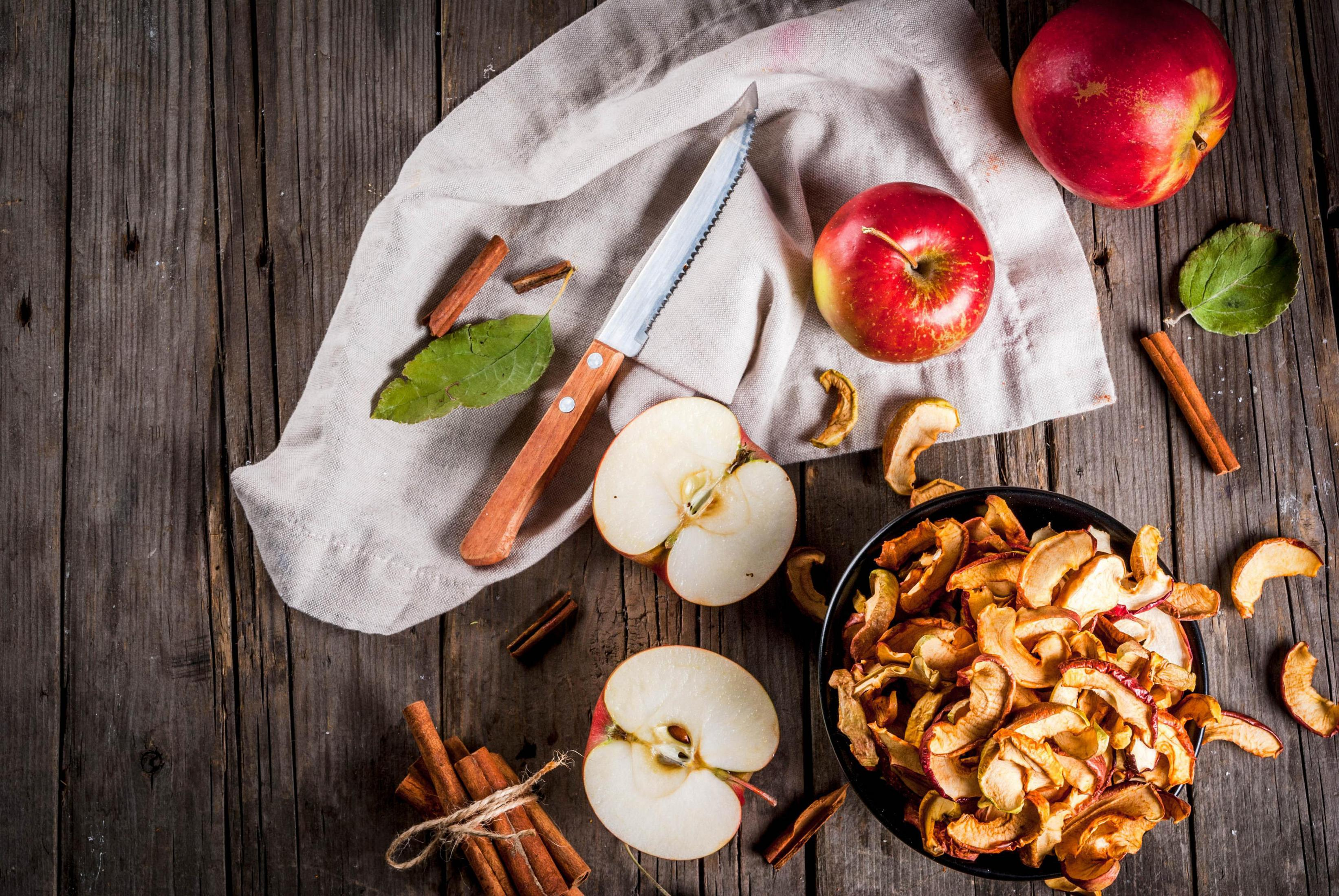 Krojone jabłka, suszone plasterki jabłka, laski cynamonu i nóż na drewnianej powierzchni.