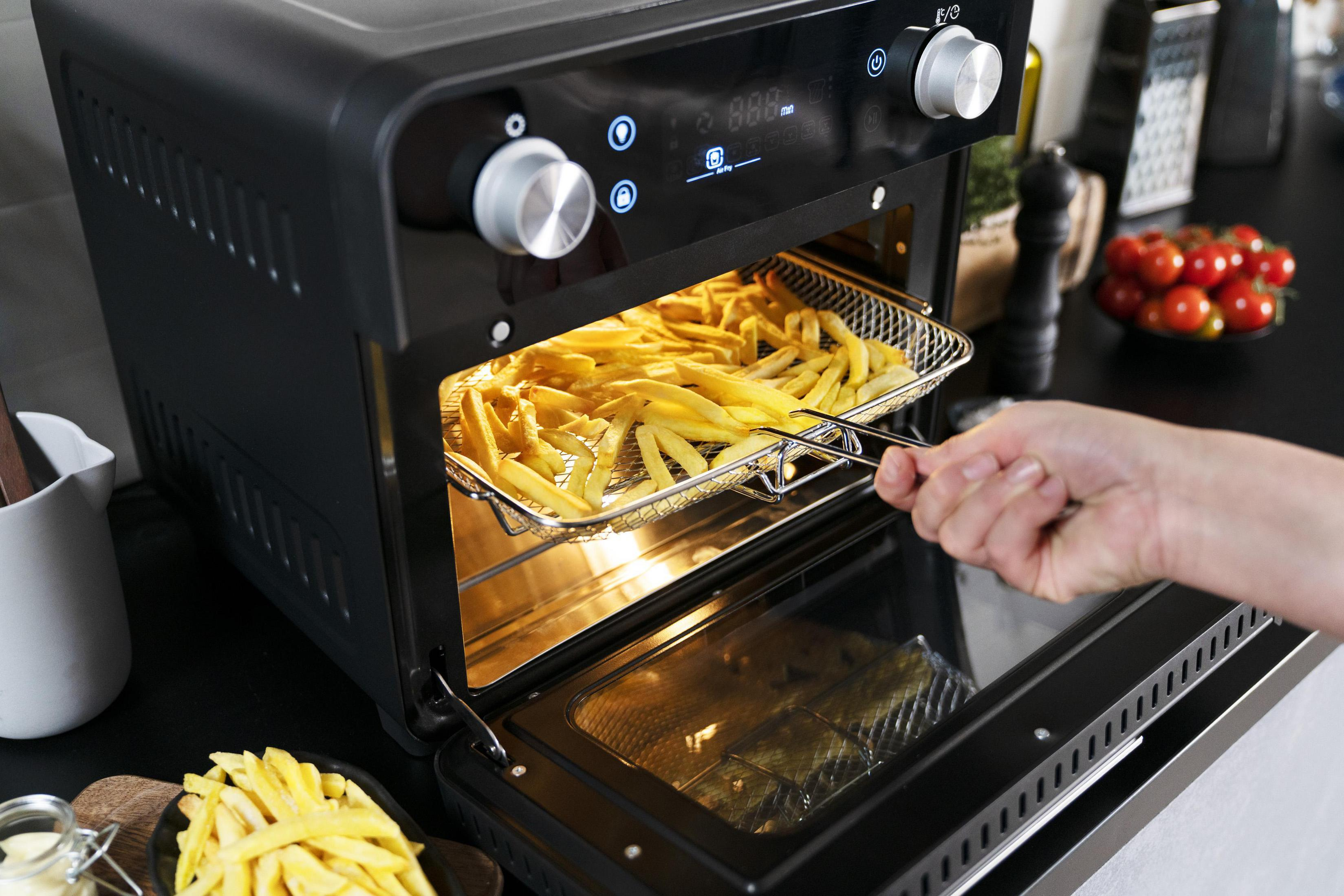 Czarna frytkownica powietrzna z frytkami wyjmowanymi z kosza. Kuchnia z ciemnym blatem.