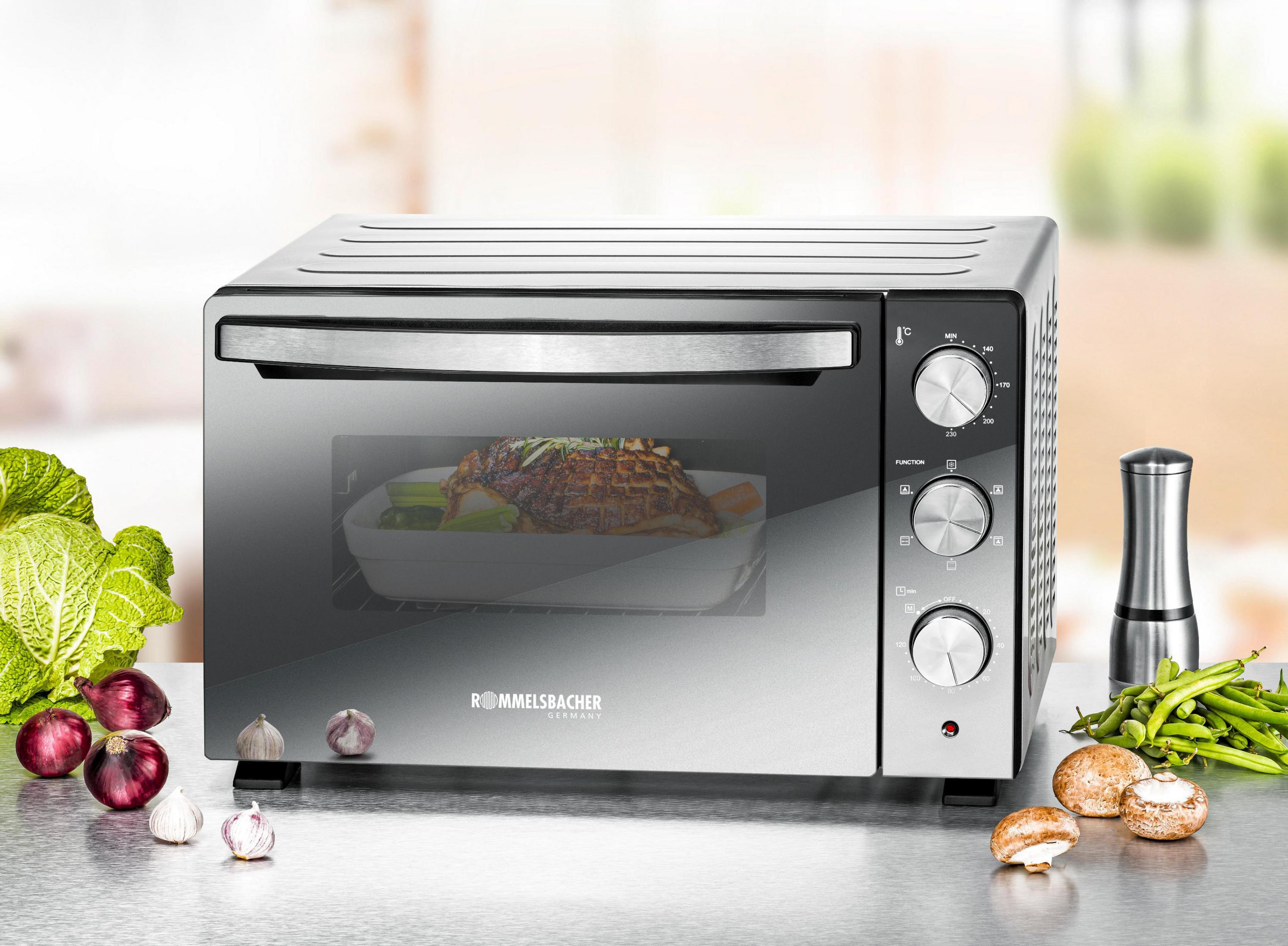 Srebrny i czarny piekarnik z jedzeniem w środku, otoczony warzywami i składnikami.