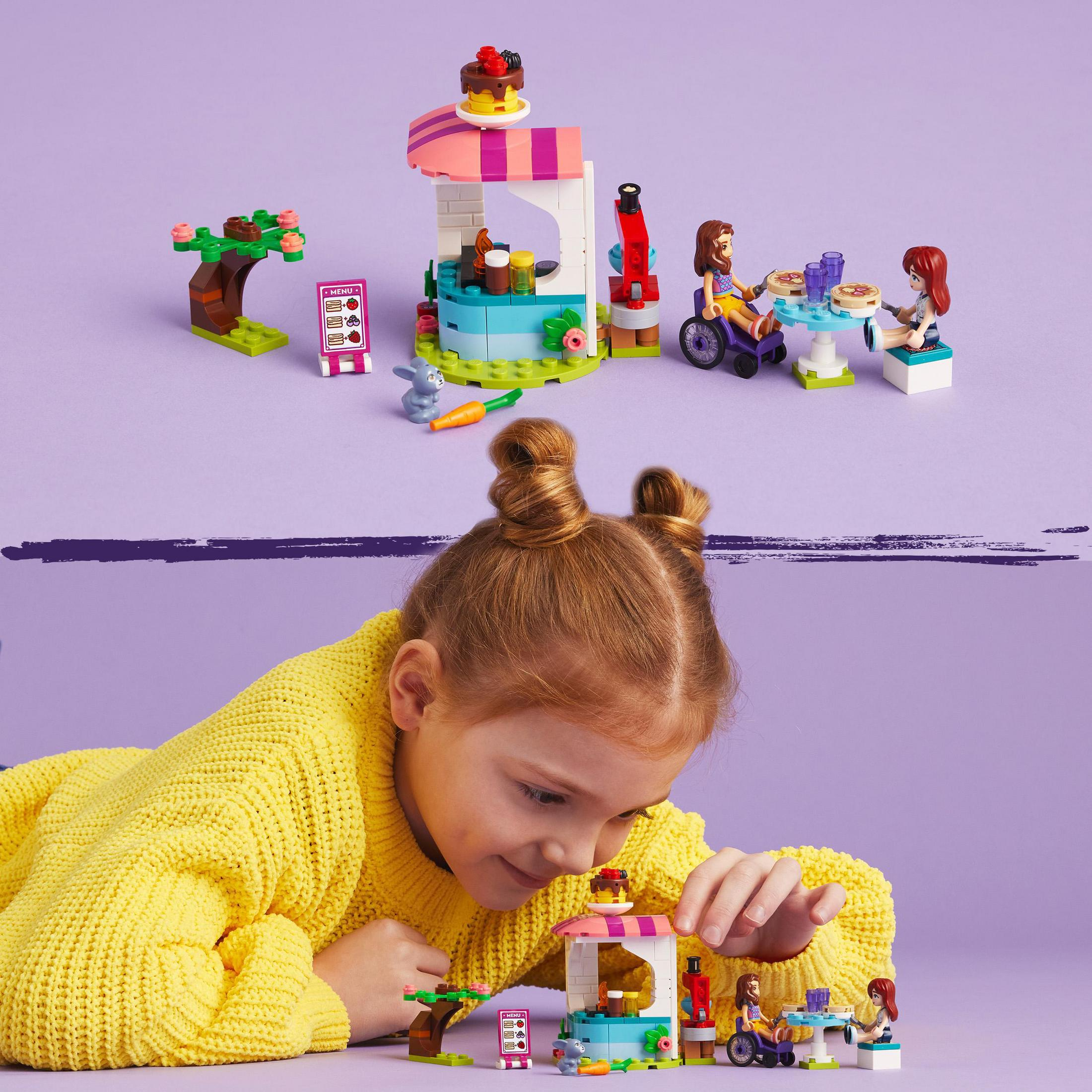 Bir kız Lego Friends seti ile oynuyor. Arka planda bir kafe ve arkadaşlar var.